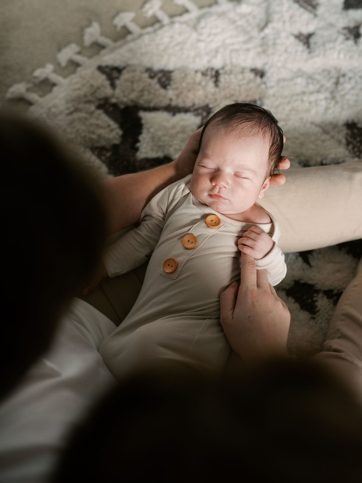 Sleeping newborn in beige onesie photographed in soft natural light.