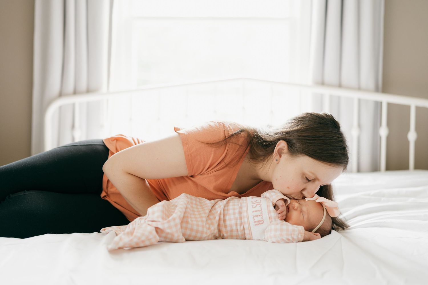 Tender moment between parent and baby lying on white bedding.