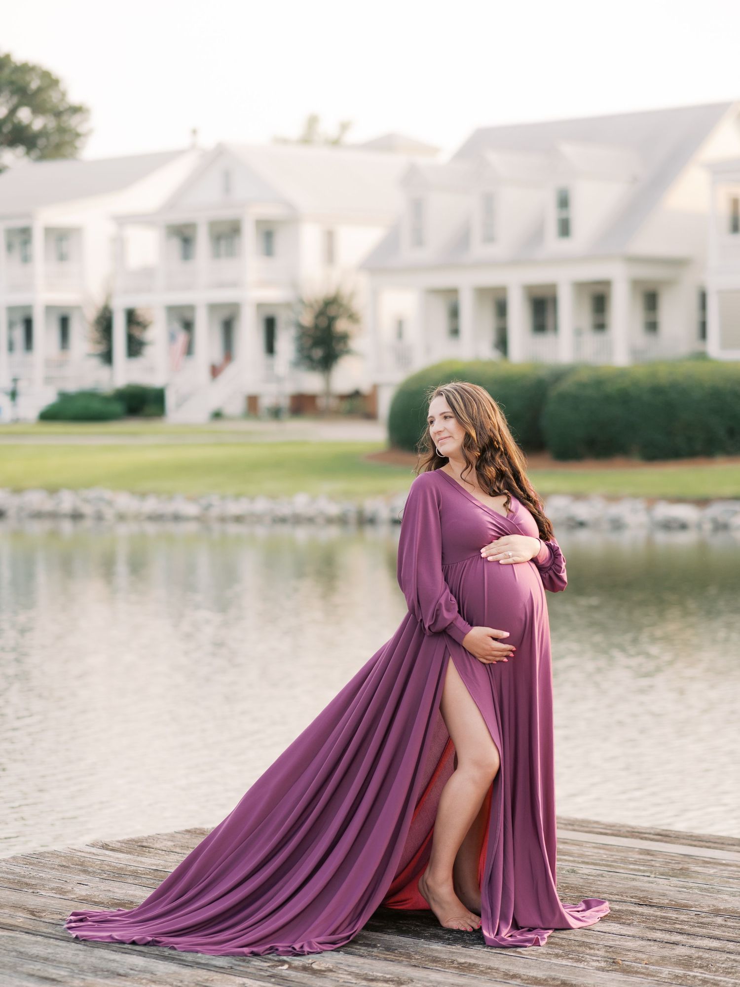 Dramatic maternity photos on a dock showing a woman in a flowing purple dress by a lakeside.