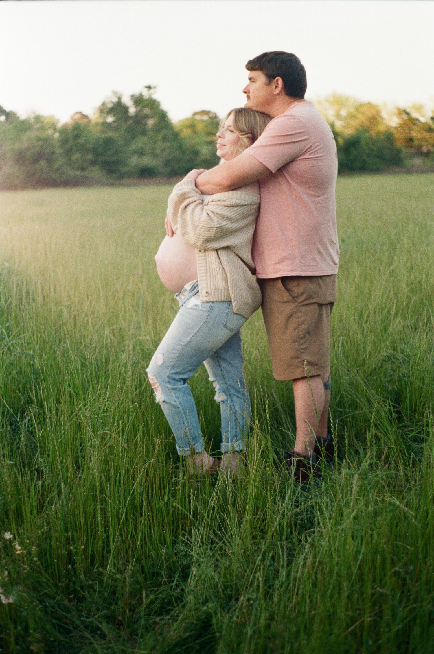 Couple embracing in tall grass field during golden hour.