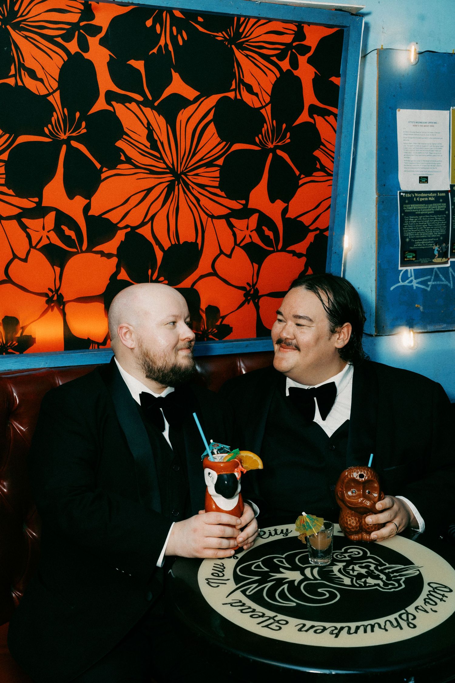 Two people dining at a table with orange floral wallpaper in the background.