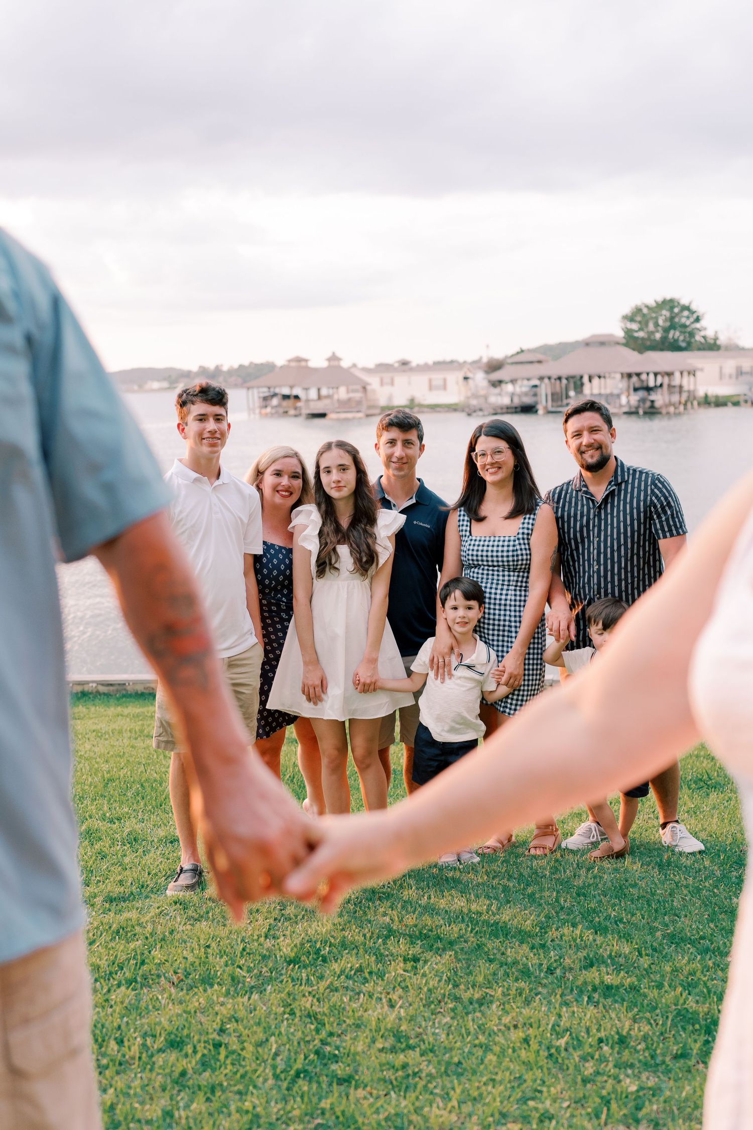 Group holding hands in a circle on grassy field with buildings in background.