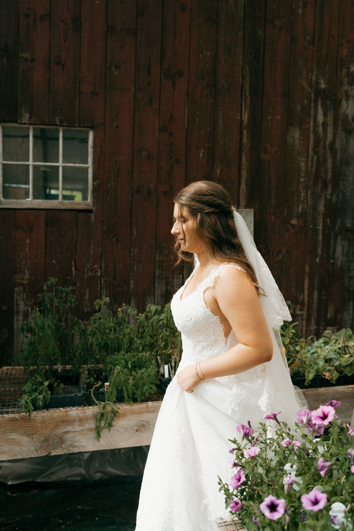 White wedding dress against rustic red barn wall with pink flowers in foreground.