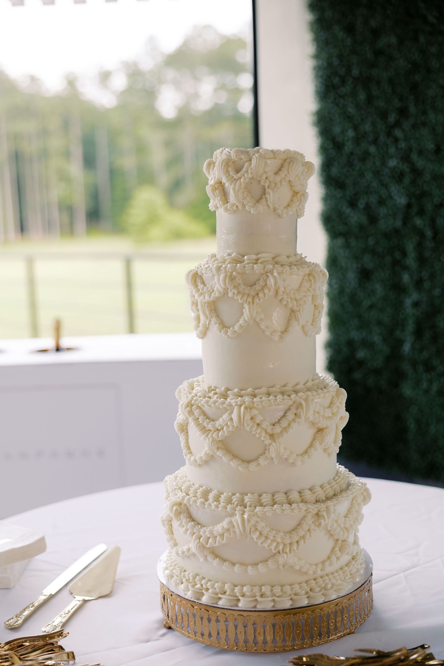 Elegant white wedding cake with intricate piped details and pearl decorations on gold base.