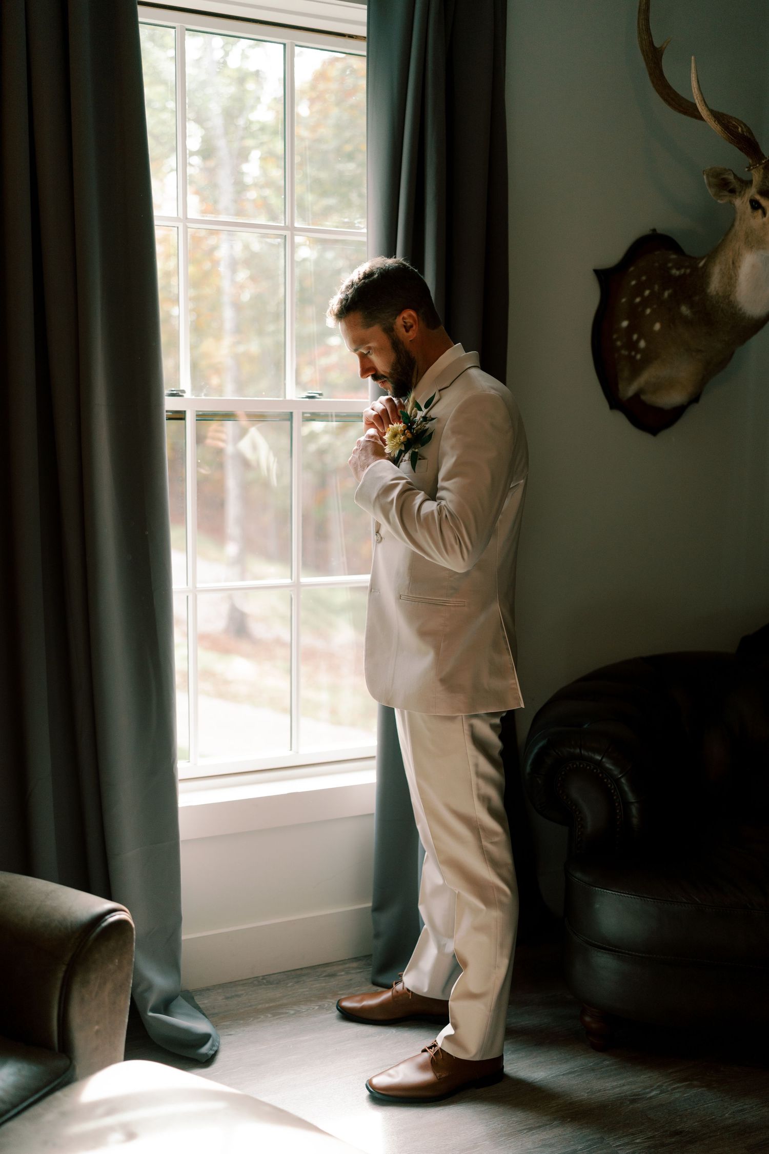 Artistic silhouette shots of groom in white suit by window with antler decor.