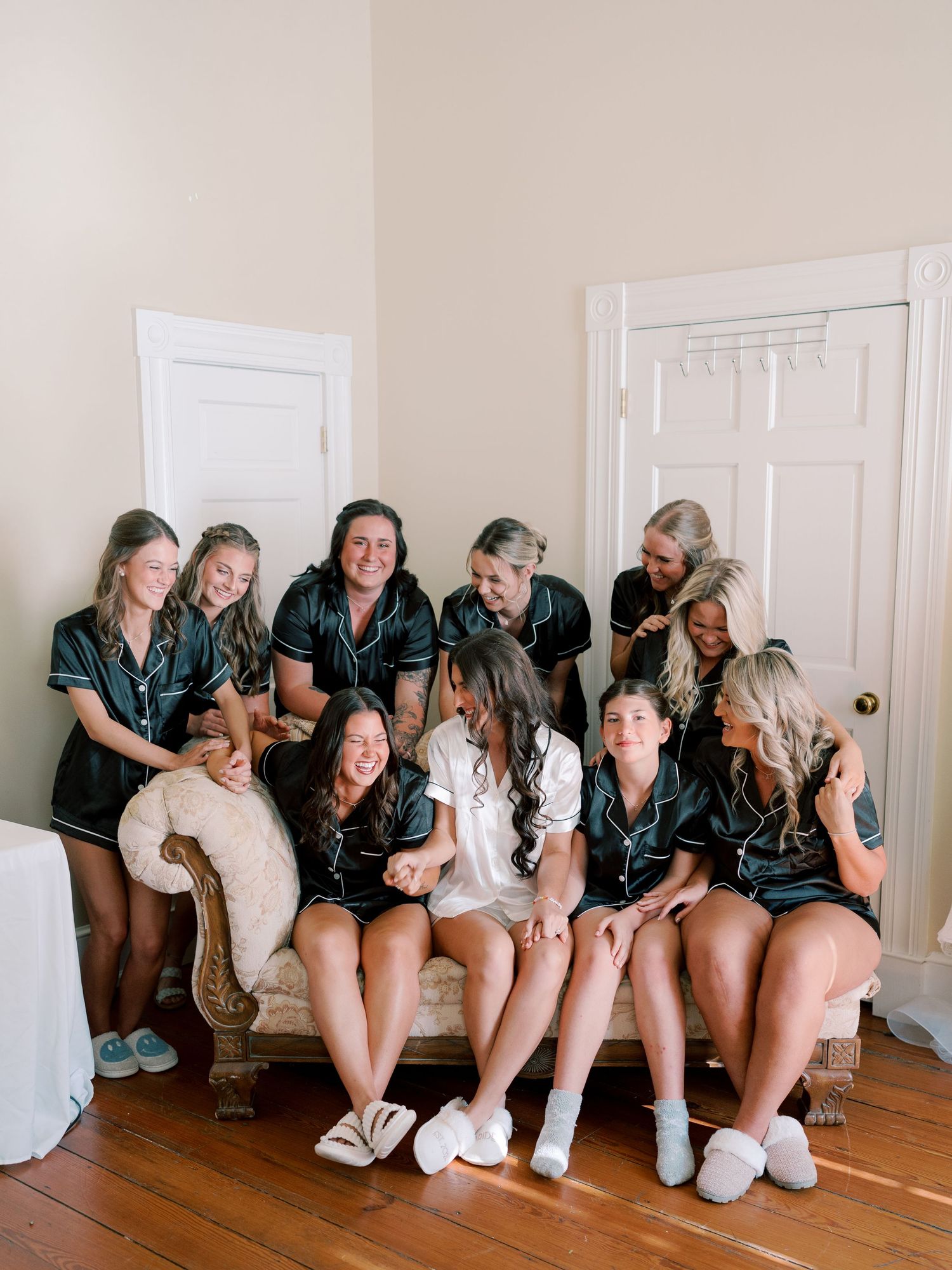 Wedding party in matching teal robes gathered on vintage couch for pre-ceremony photos.