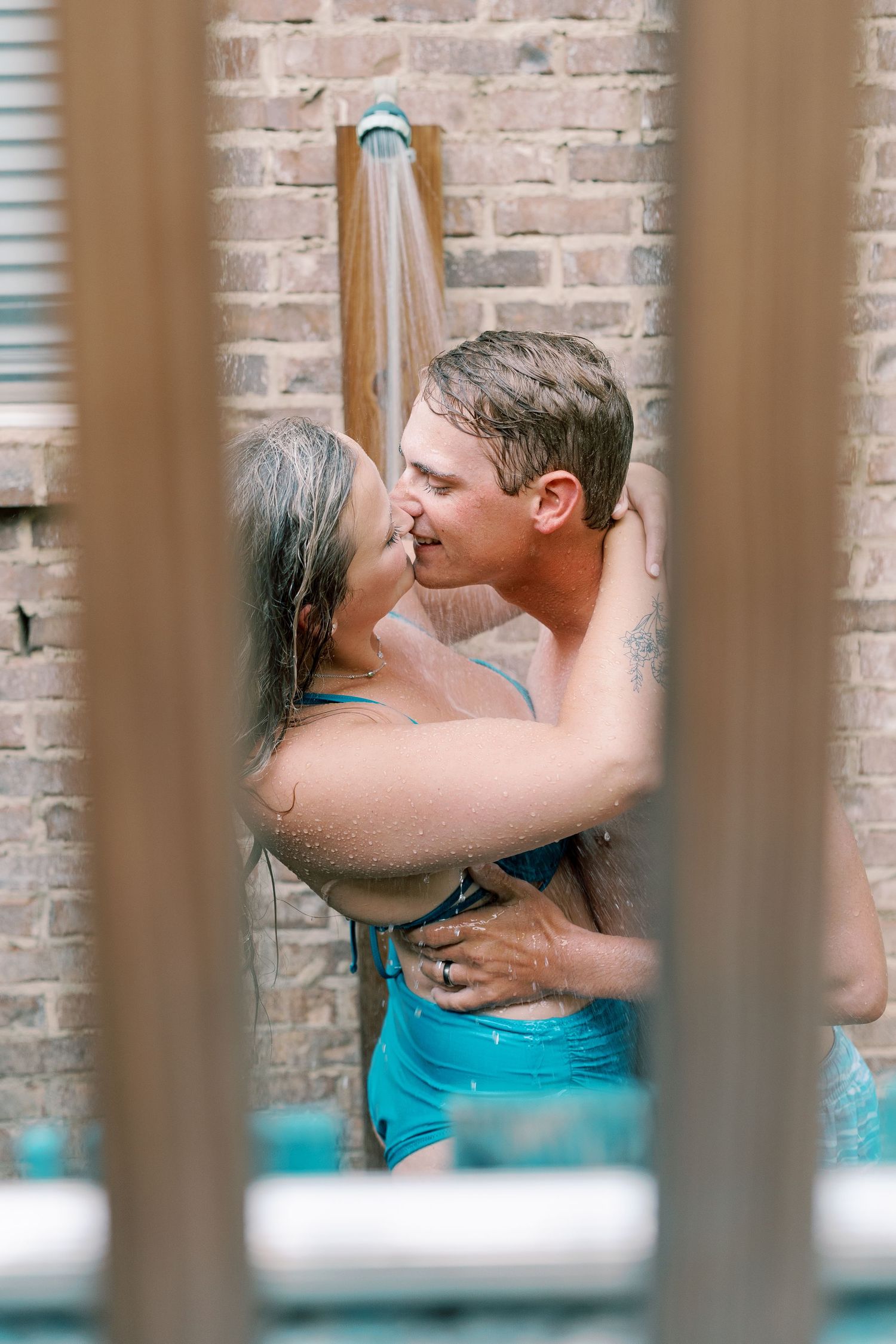 Romantic couple embraces against brick wall viewed through vertical bars in intimate moment.