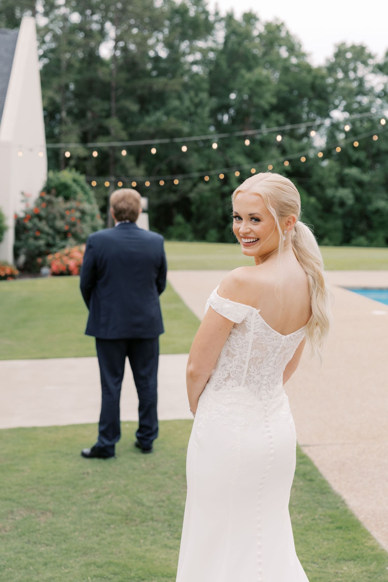 Bride in a stunning white wedding dress poses outdoors with string lights in the background.