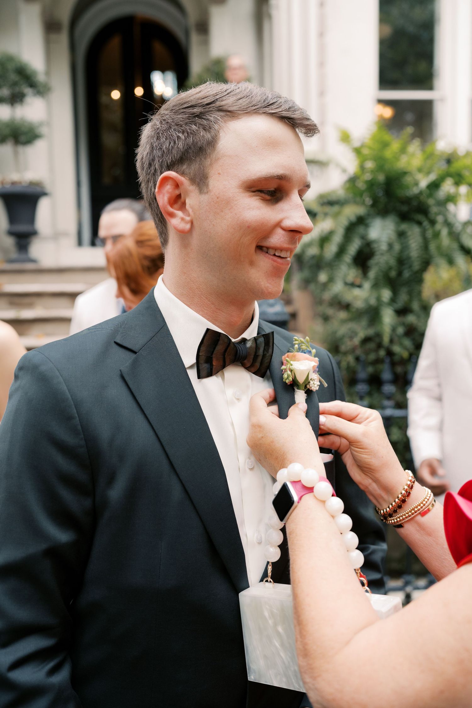 Formal wedding preparations showing suit adjustments and boutonniere pinning.