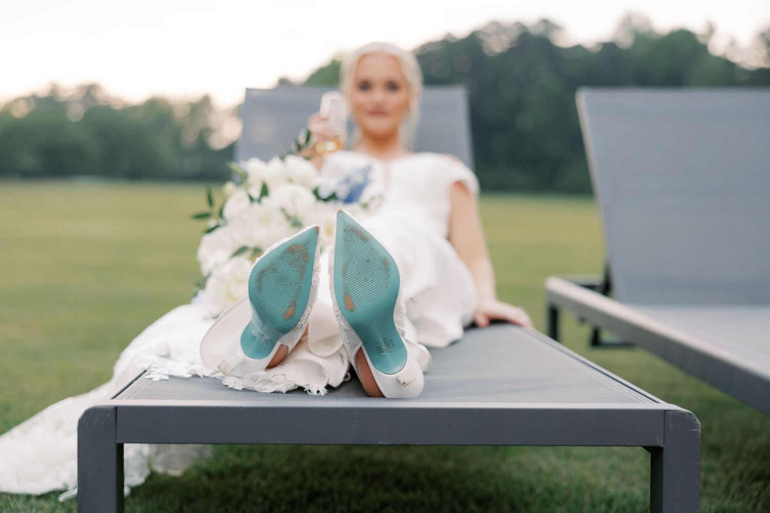 Elegant bridal shoes with turquoise soles displayed on a modern bench at an outdoor wedding venue.