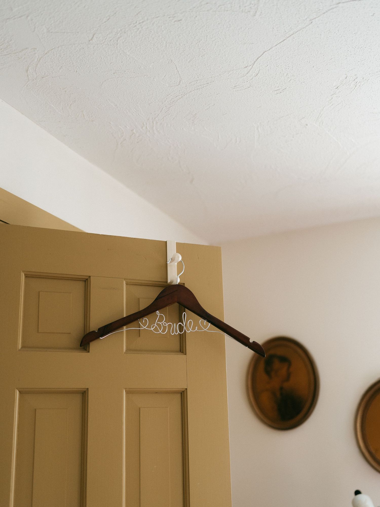 Wooden wedding dress hanger displayed against a beige door with decorative wall plates.
