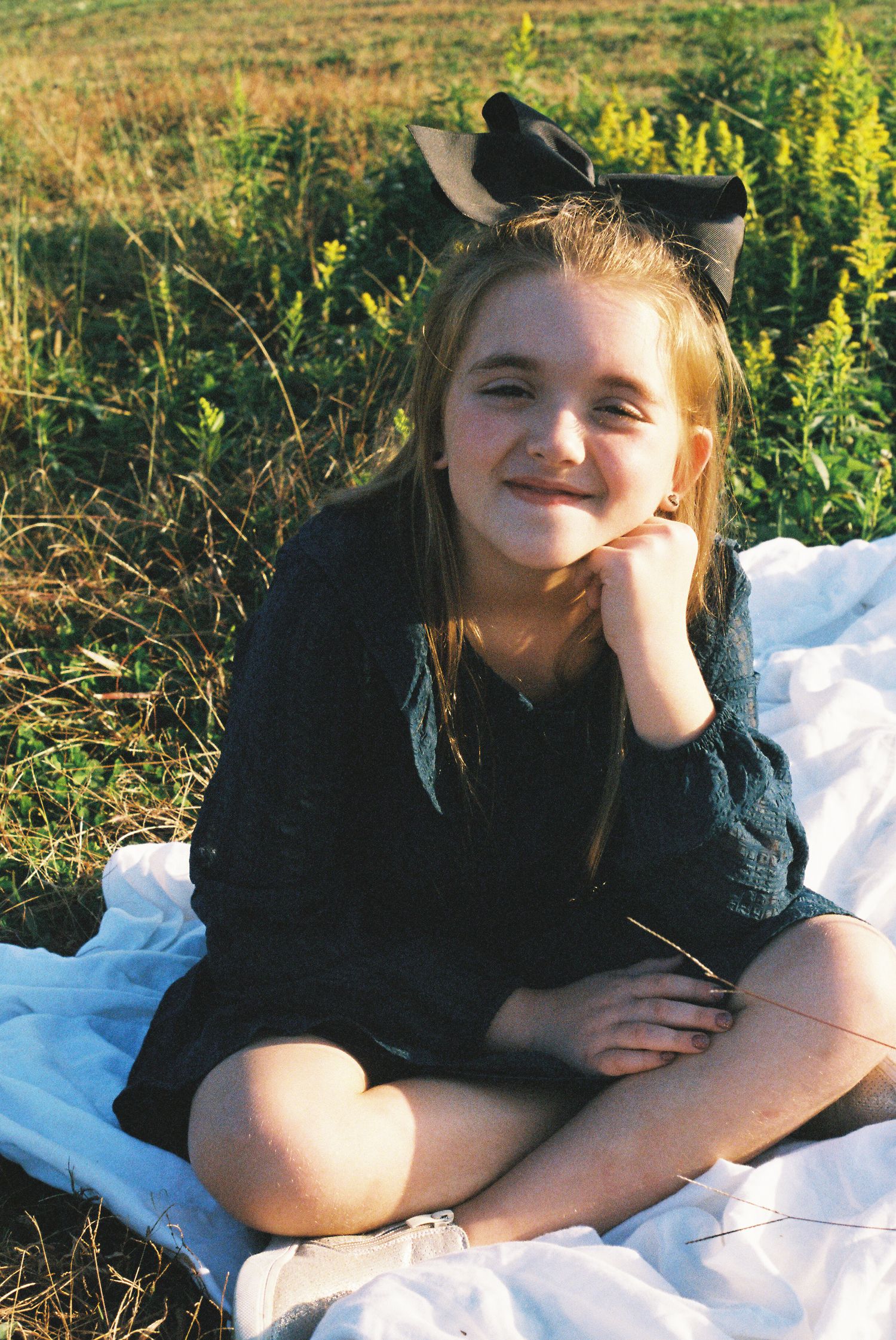 Person lying on a white blanket outdoors in grassy field with yellow wildflowers in background.