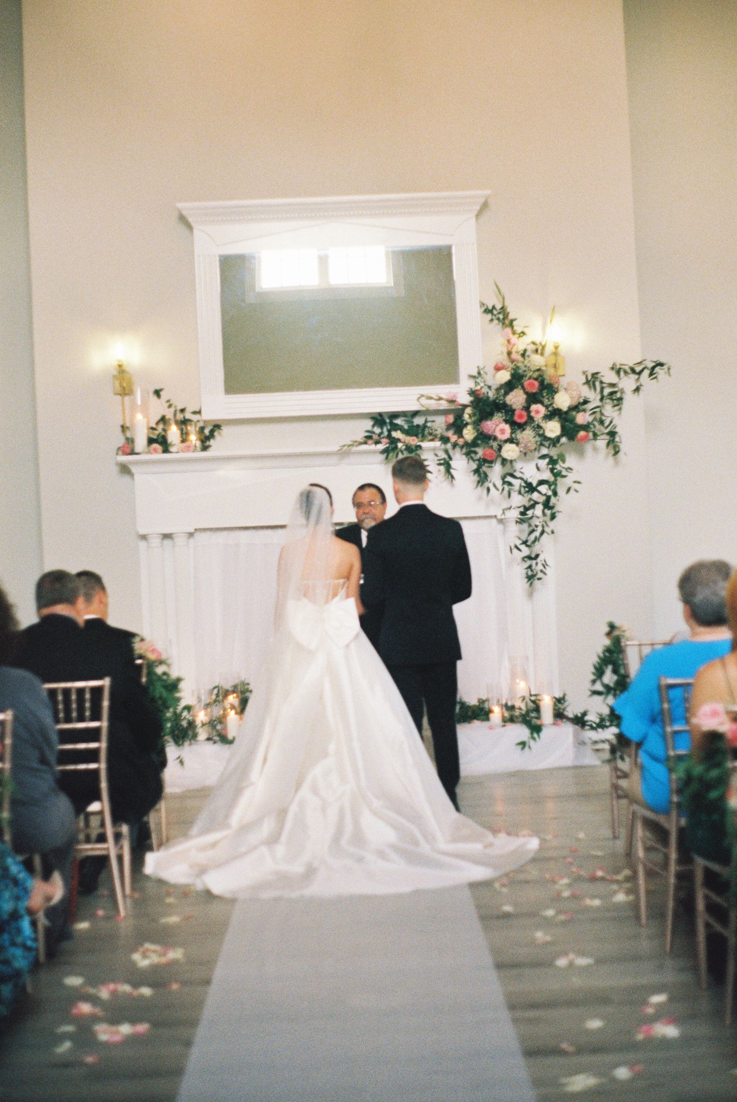Wedding ceremony setup in an indoor venue with white chairs and floral decorations.