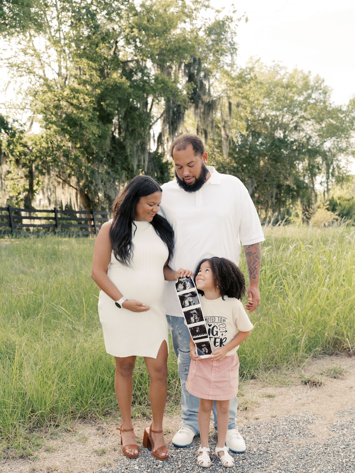 A family poses with ultrasound photos in a natural outdoor setting.