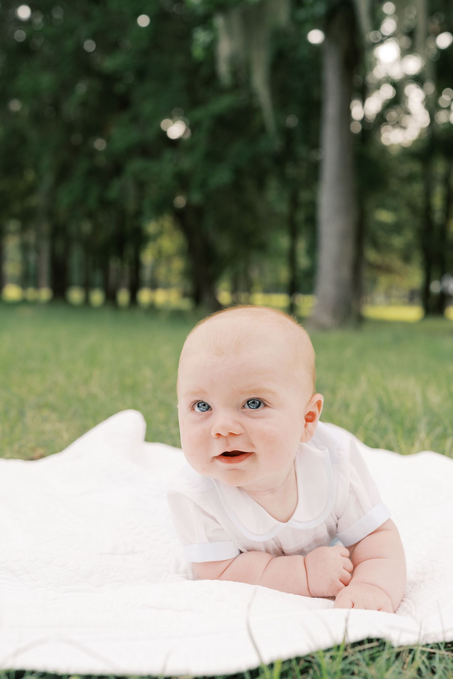 Baby with bright blue eyes laying on white blanket during outdoor photo session.