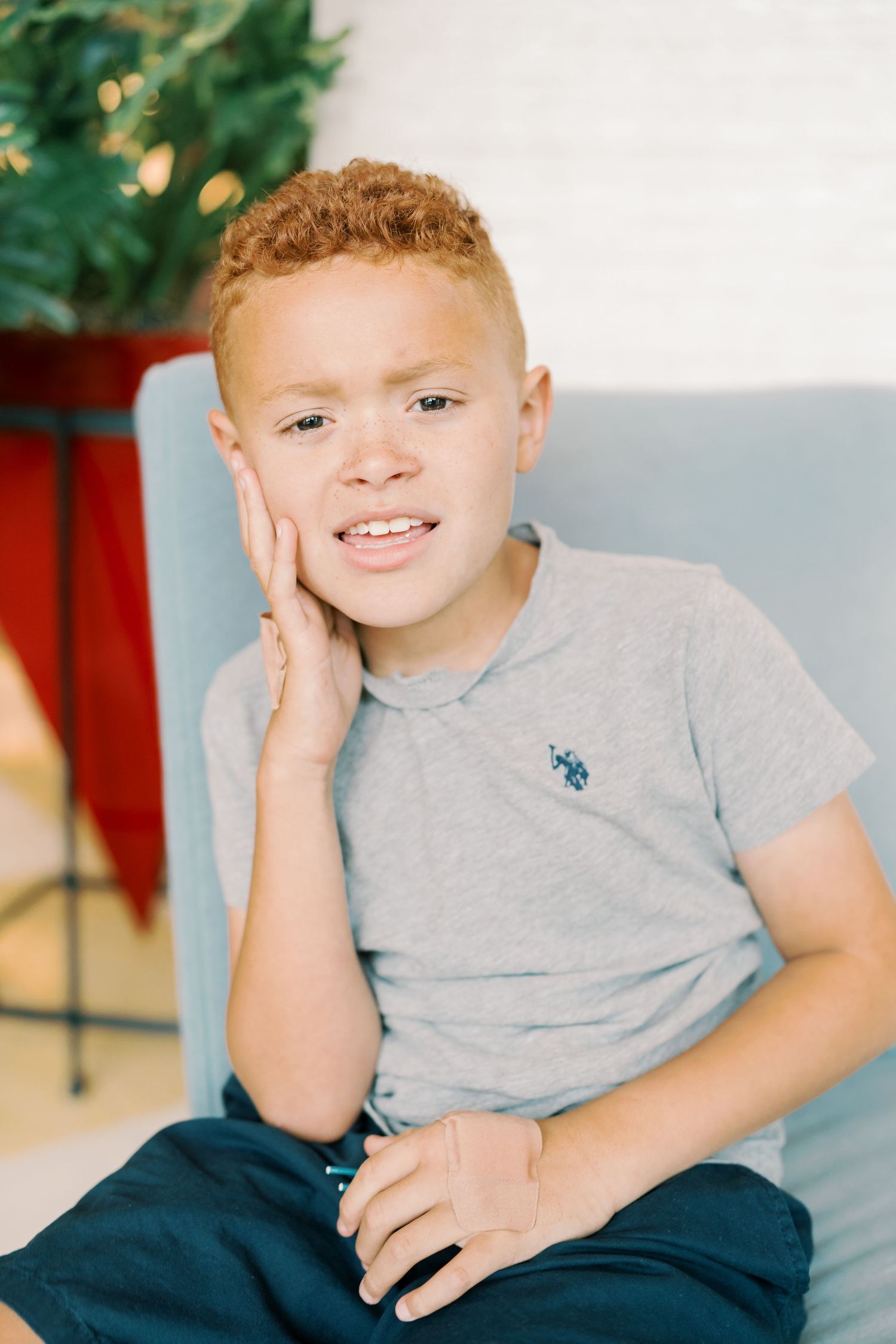 Child in grey t-shirt sitting casually against light background.