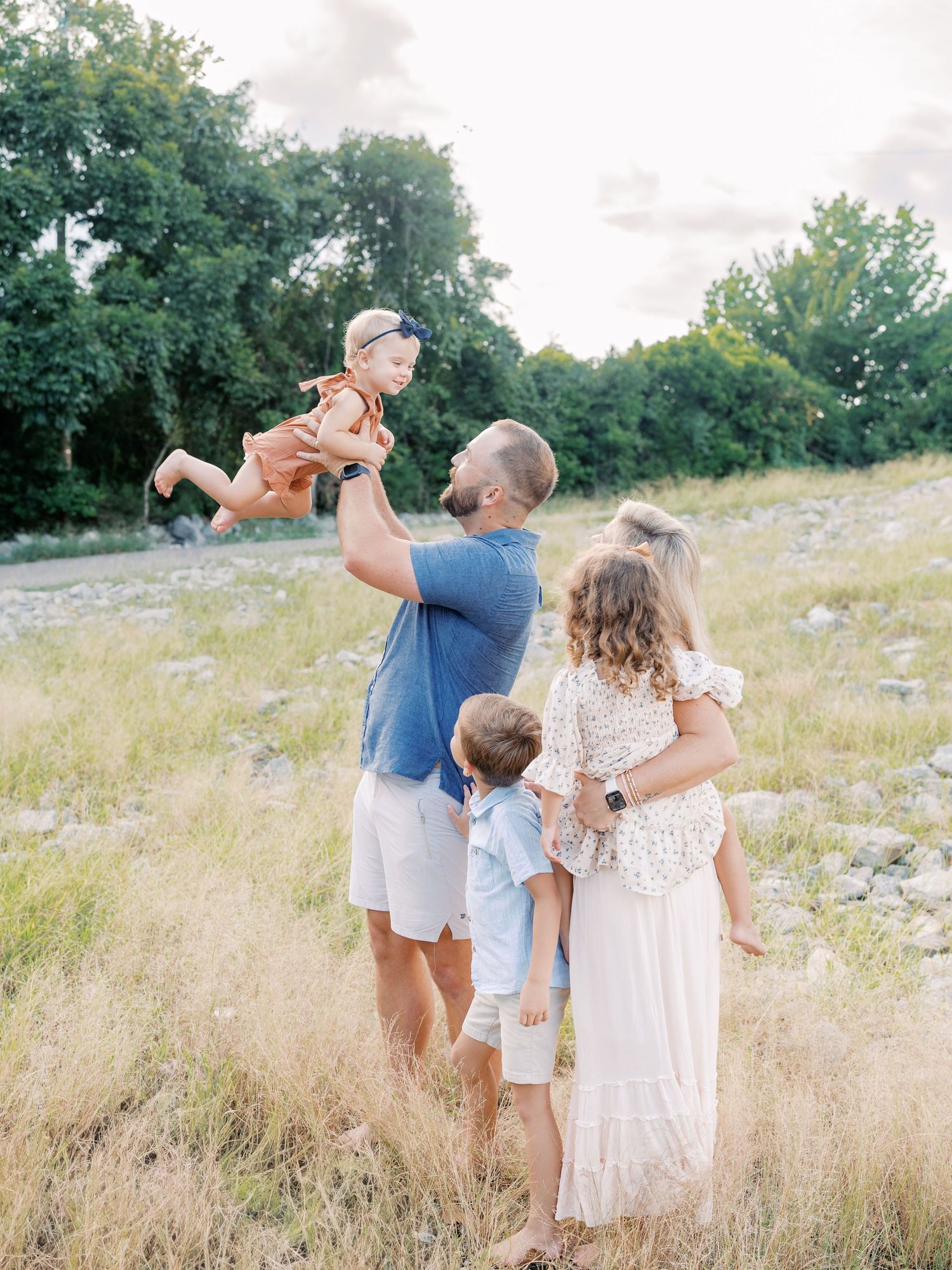 A family enjoys playful moments together in a grassy field on a bright summer day.