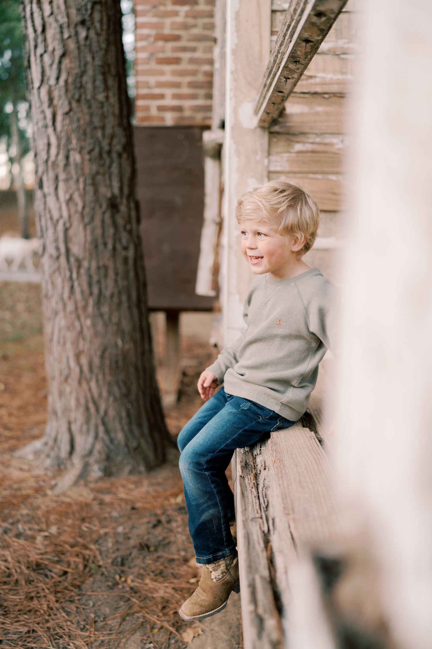 A child in a gray sweater sits on a wooden ledge next to a brick building.