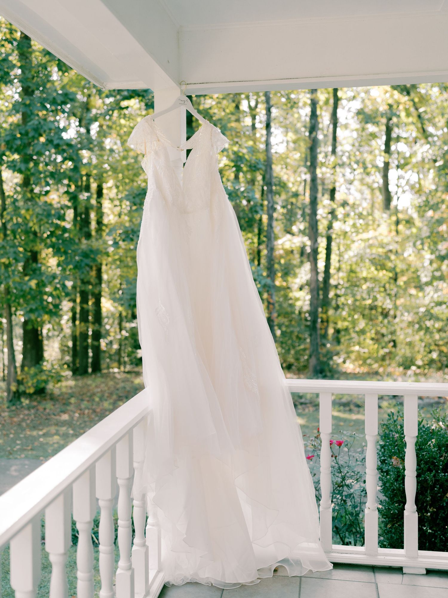 White wedding dress hanging on porch railing with forest backdrop.