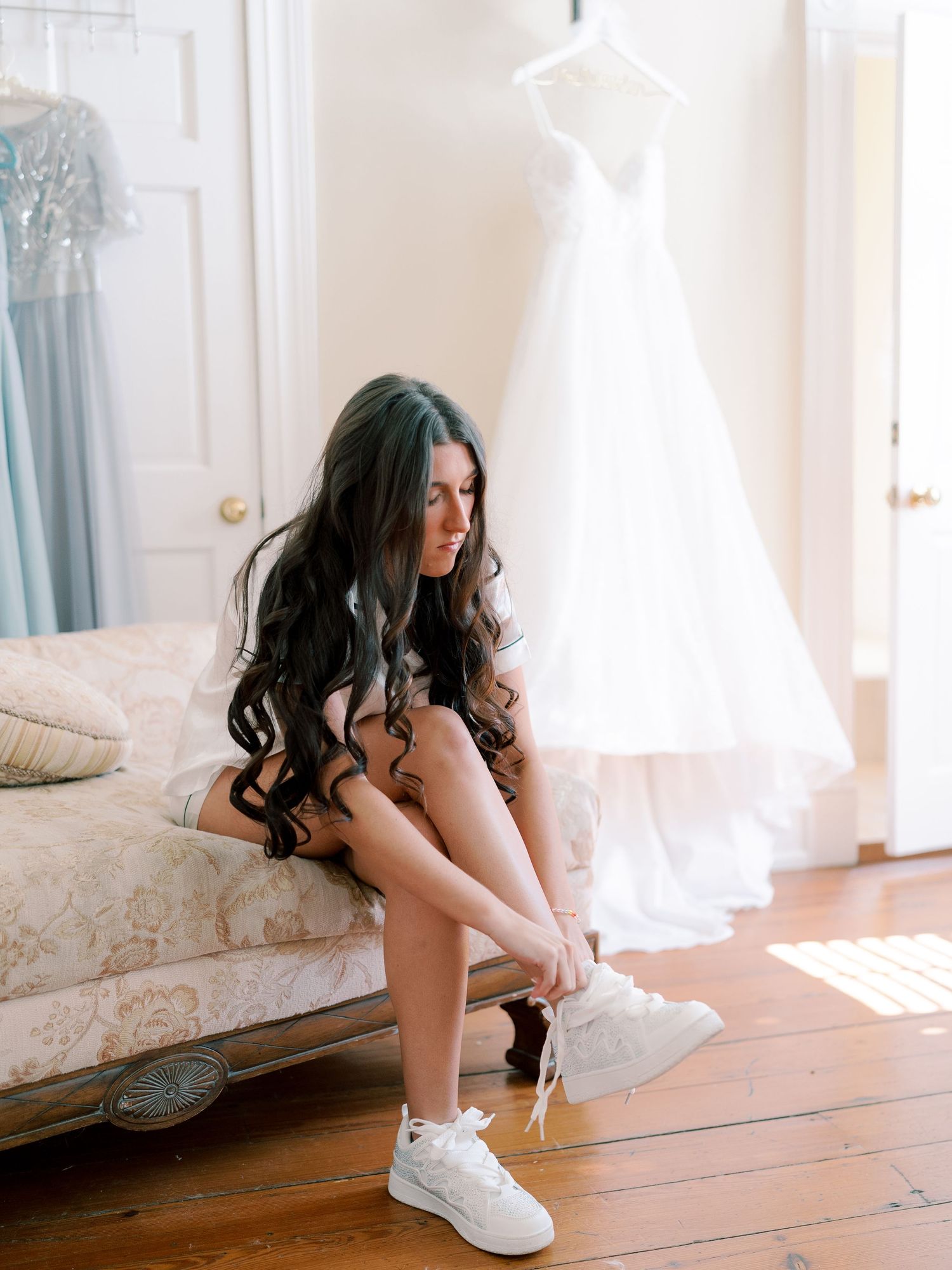 Getting ready scene with white sneakers and wedding dress hanging in background.