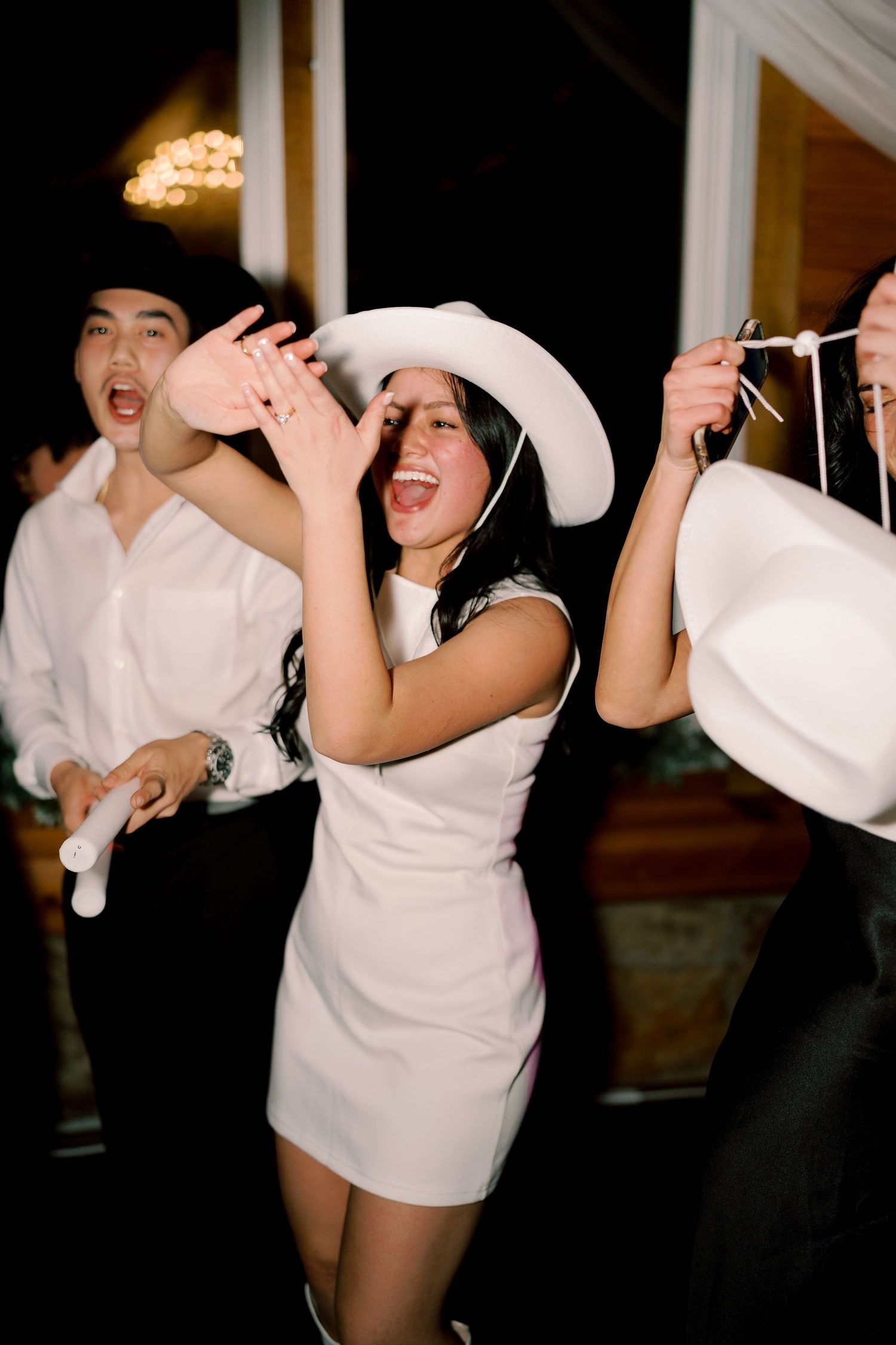 People in white cowboy hats and dresses dancing and having fun at a party.