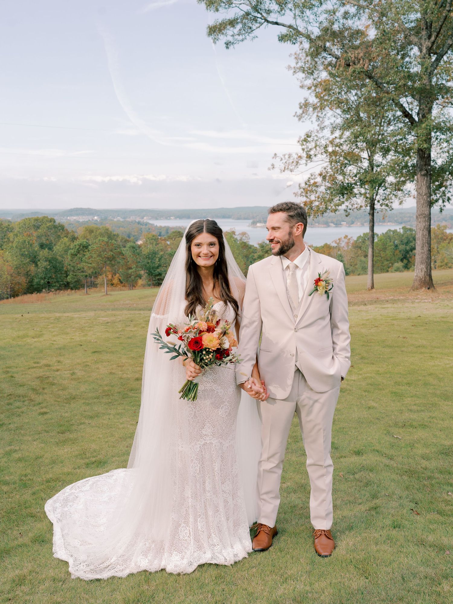 Newlyweds walking through scenic outdoor venue in cream suit and lace wedding gown.