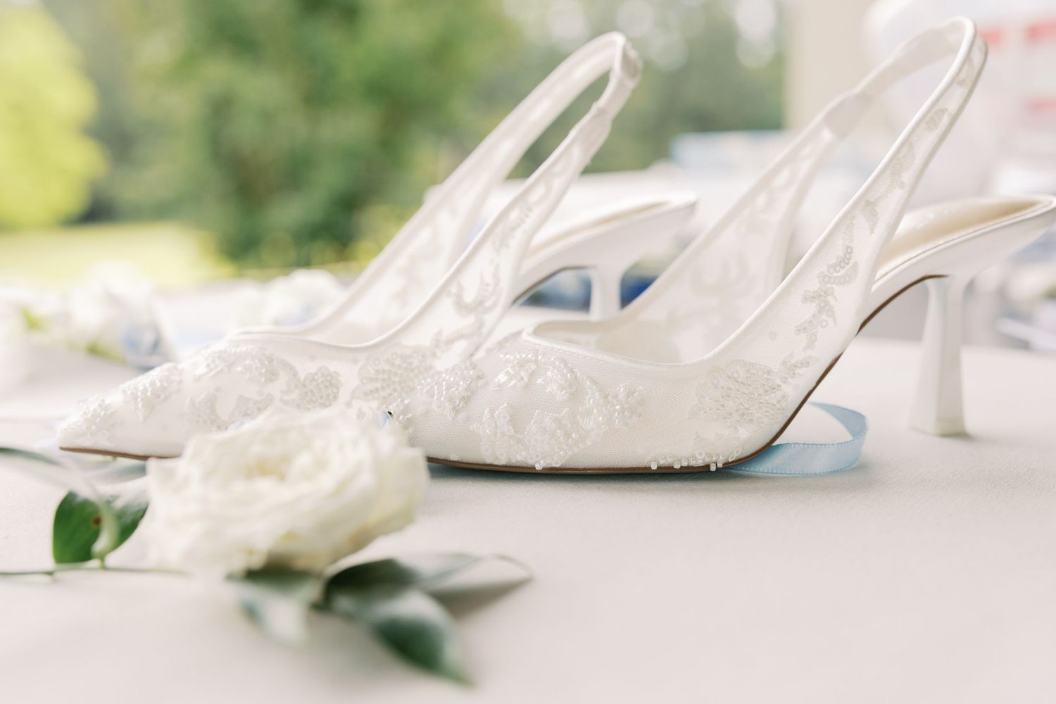 Close-up of elegant white bridal heels arranged with flowers on a light surface.
