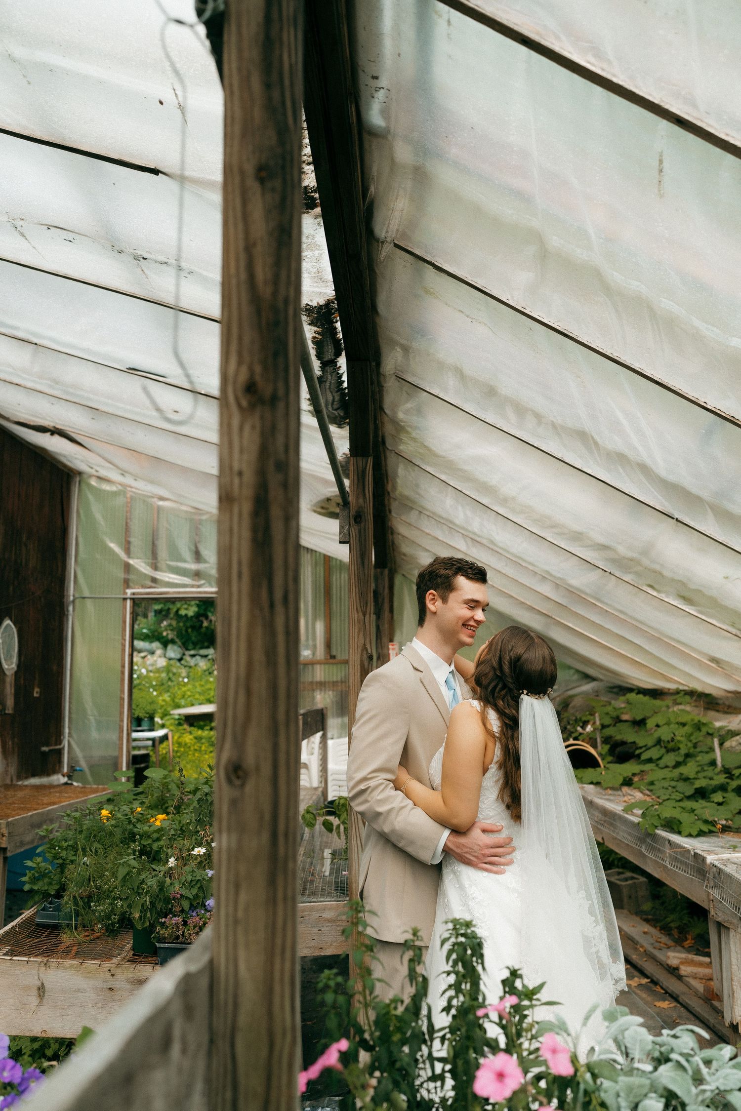 Intimate wedding portrait under greenhouse panels with pink and purple flowers.