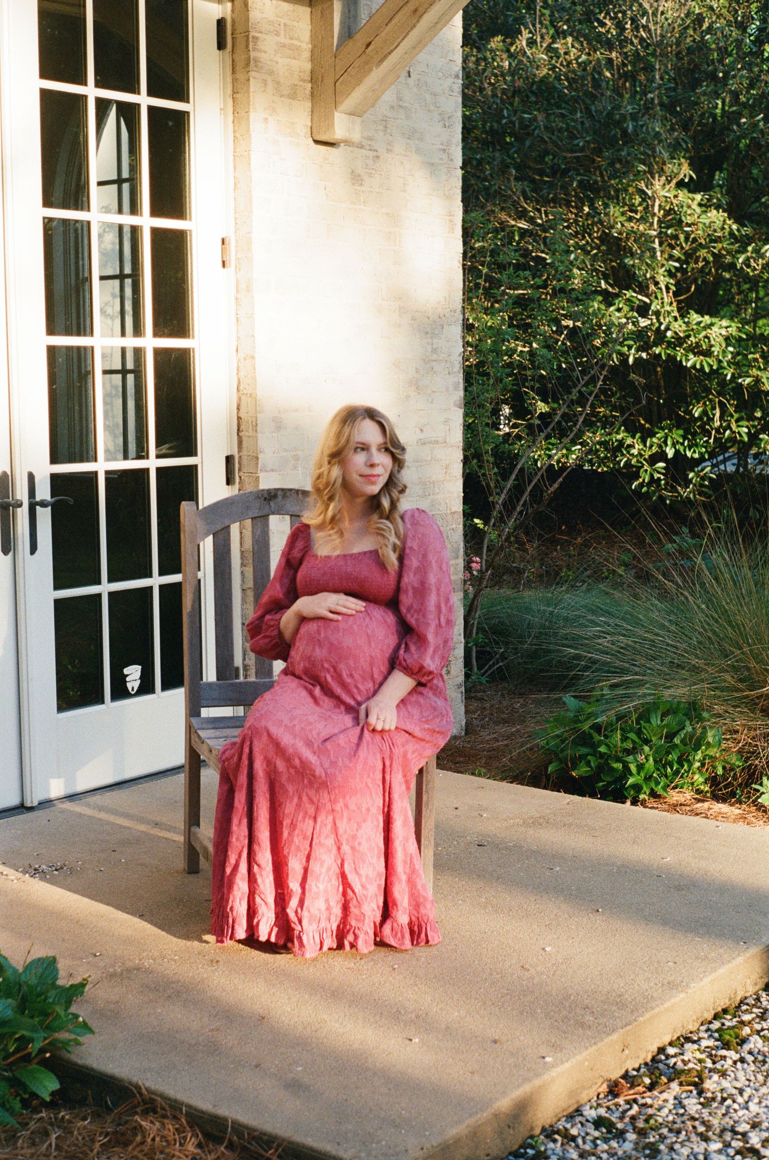 Woman in pink vintage dress sitting on white porch with French doors.
