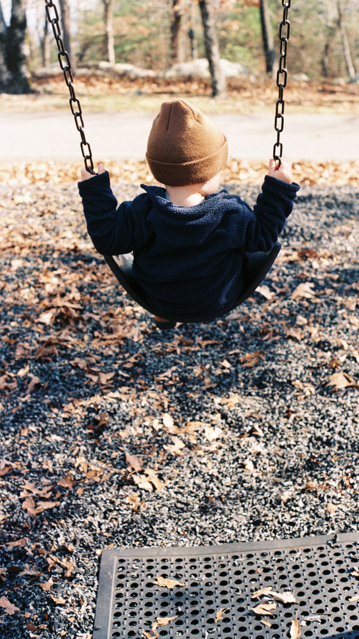 Child wearing a brown beanie swinging on a playground swing set during autumn.
