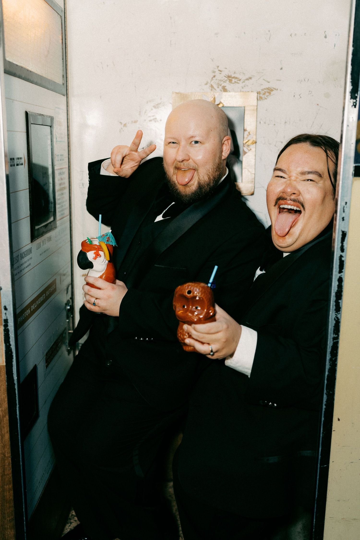 Two people in formal attire laughing and posing with drinks.