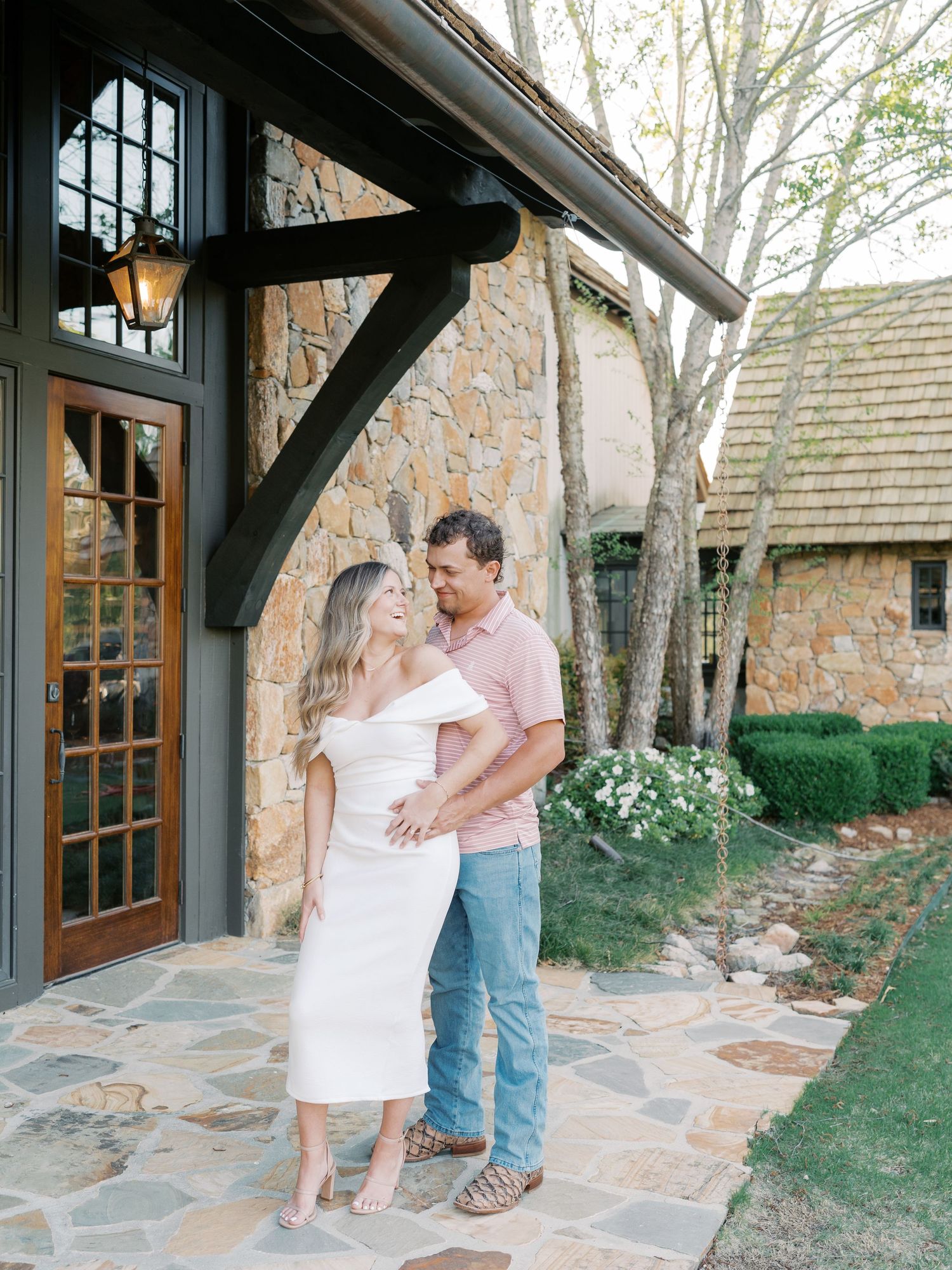 Dancing couple shares playful moments on stone patio outside rustic building.