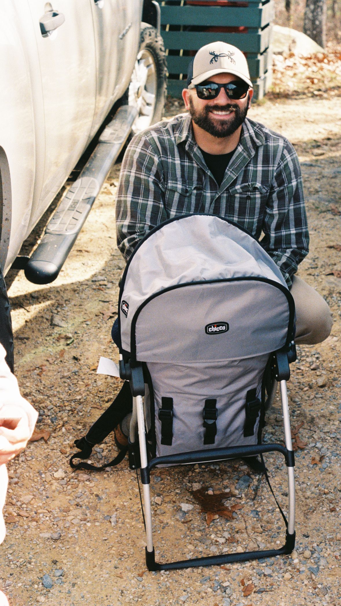 Person sitting in a gray camping chair outdoors wearing plaid and sunglasses.