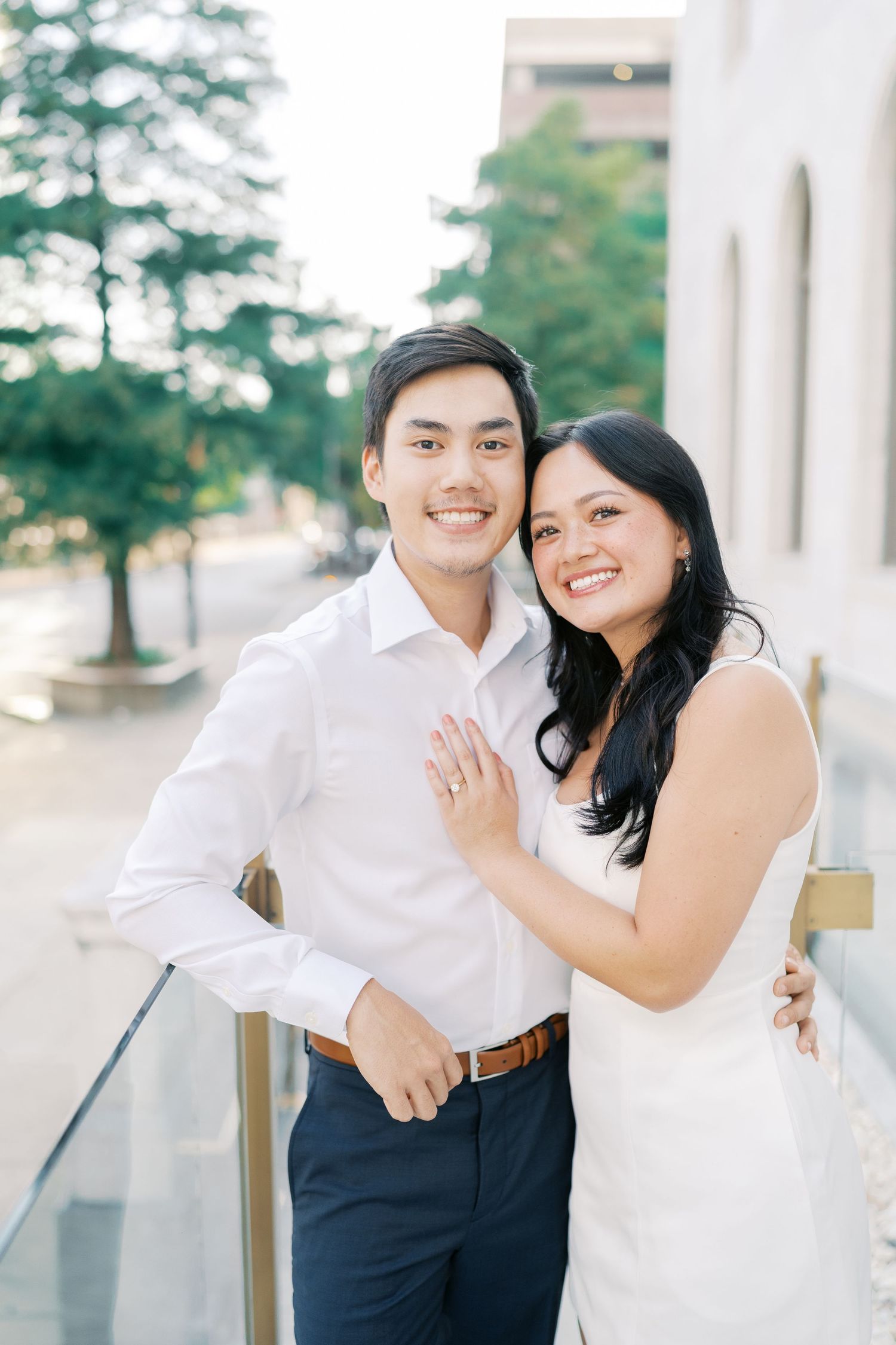 A couple shares a tender moment while posing together outdoors near white architectural columns.