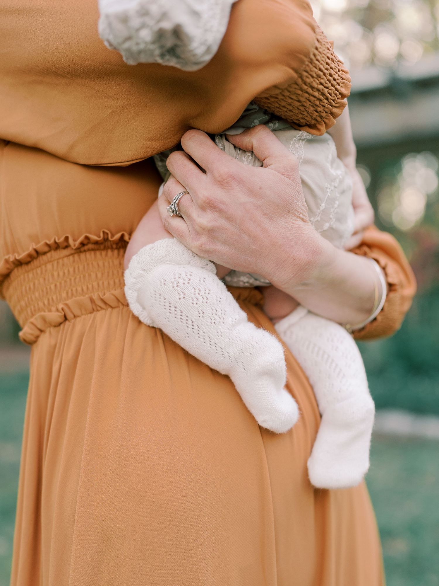 Close-up shots of a baby in white lace being held against rust-colored fabric.