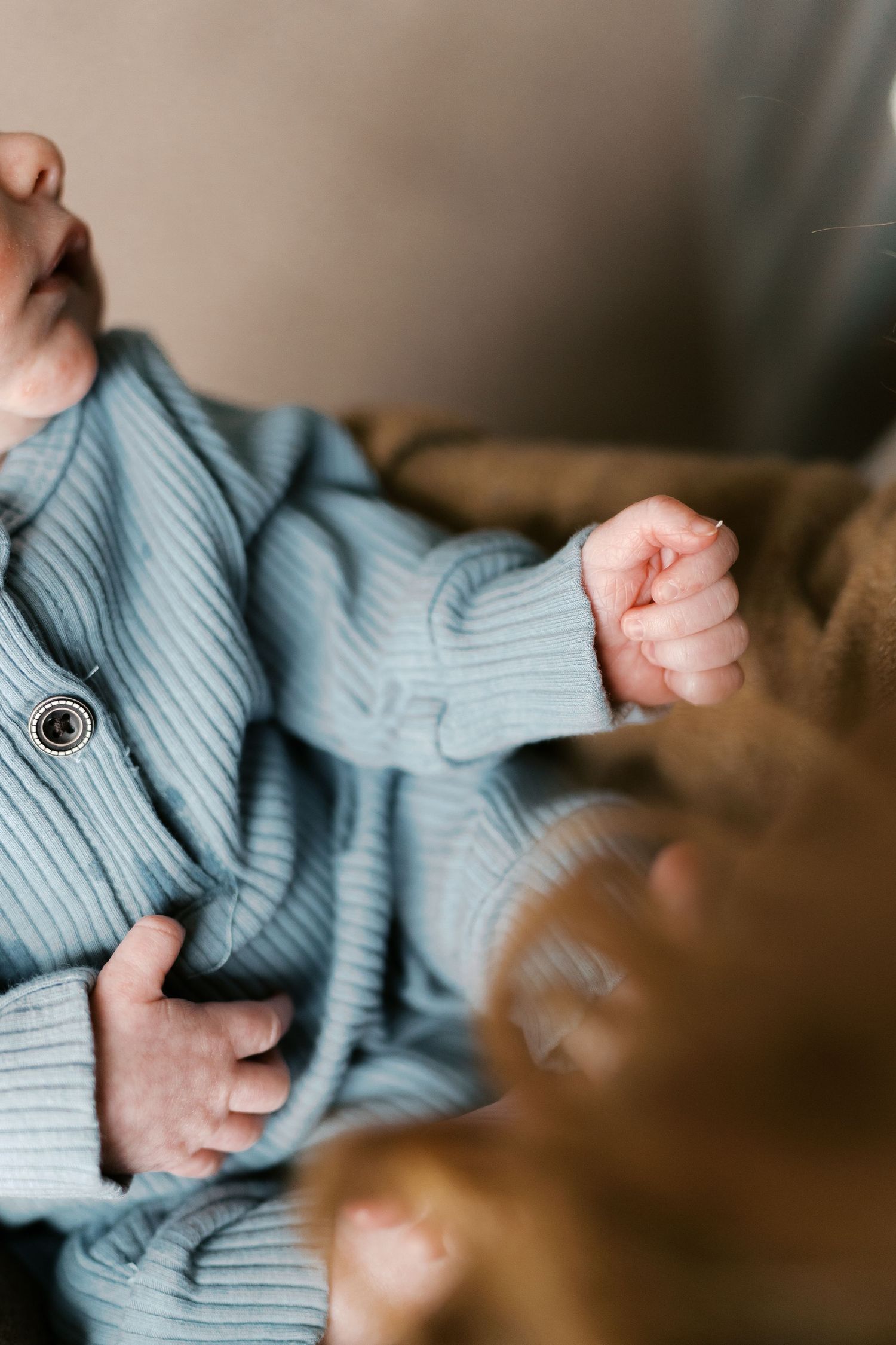 Close-up of tiny fingers grasping a light blue knit sweater in soft natural lighting.