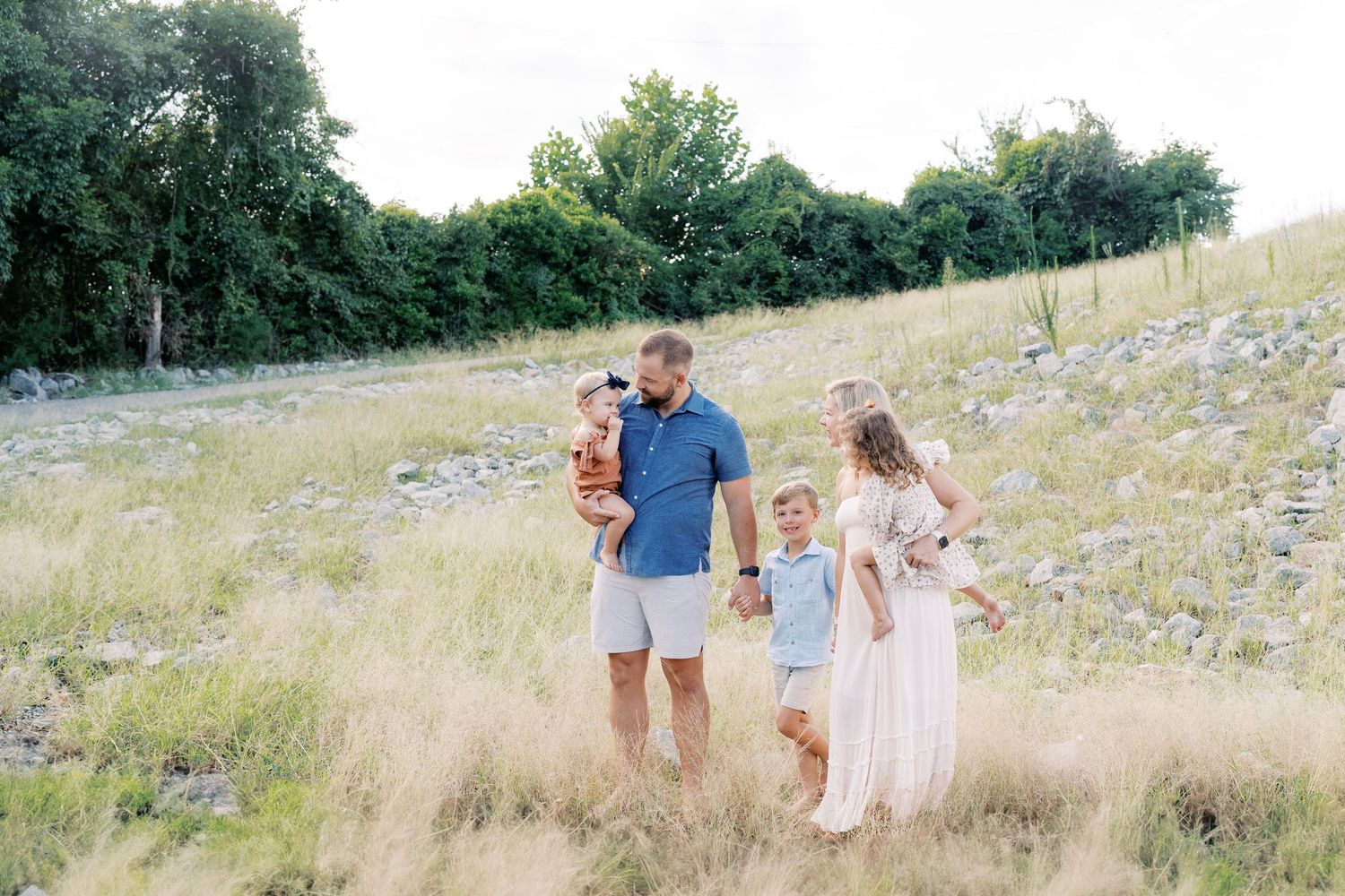 A family walks together through a scenic meadow on a bright afternoon.