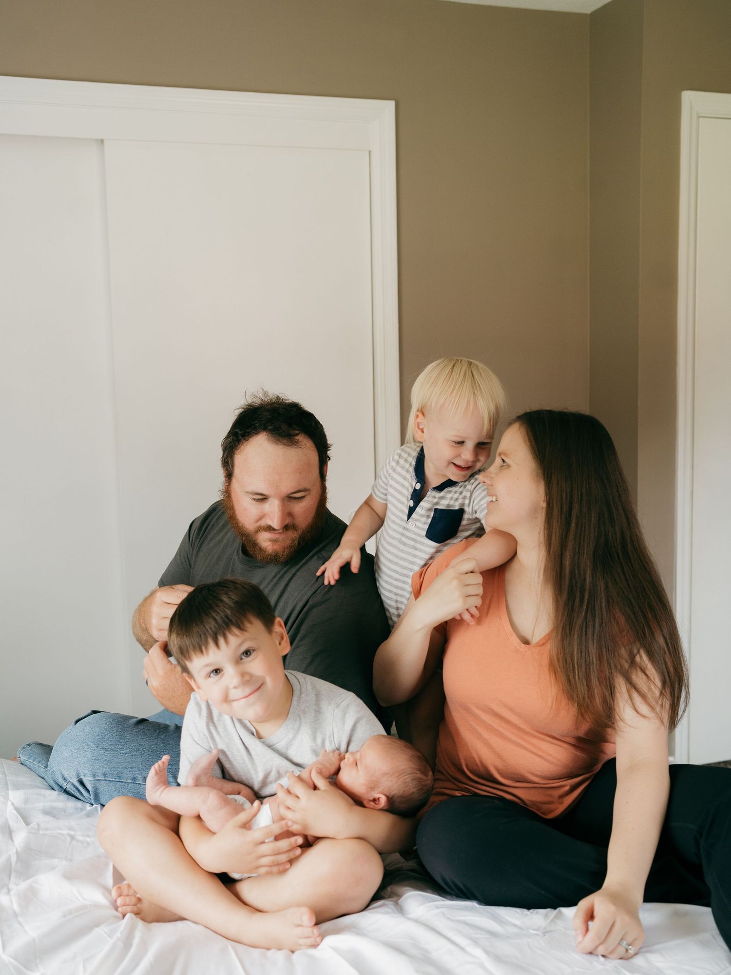 Candid family moment captured on white bed during indoor photoshoot.