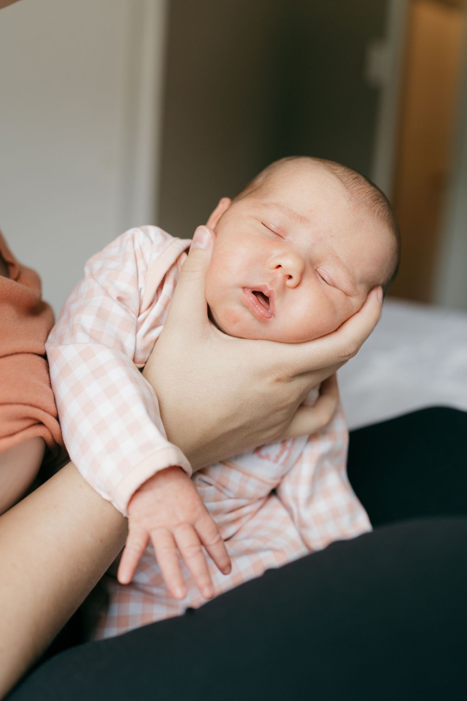 Sleeping infant in pink and white patterned outfit being gently held.
