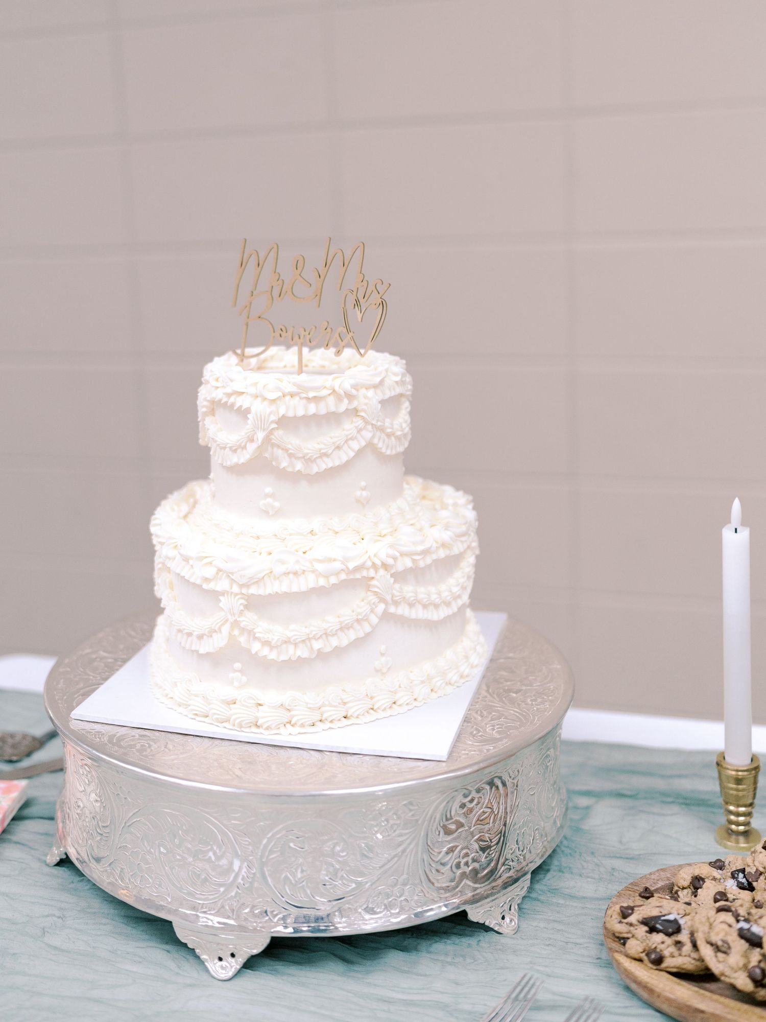 Classic white three-tier wedding cake with delicate piping on a silver cake stand.