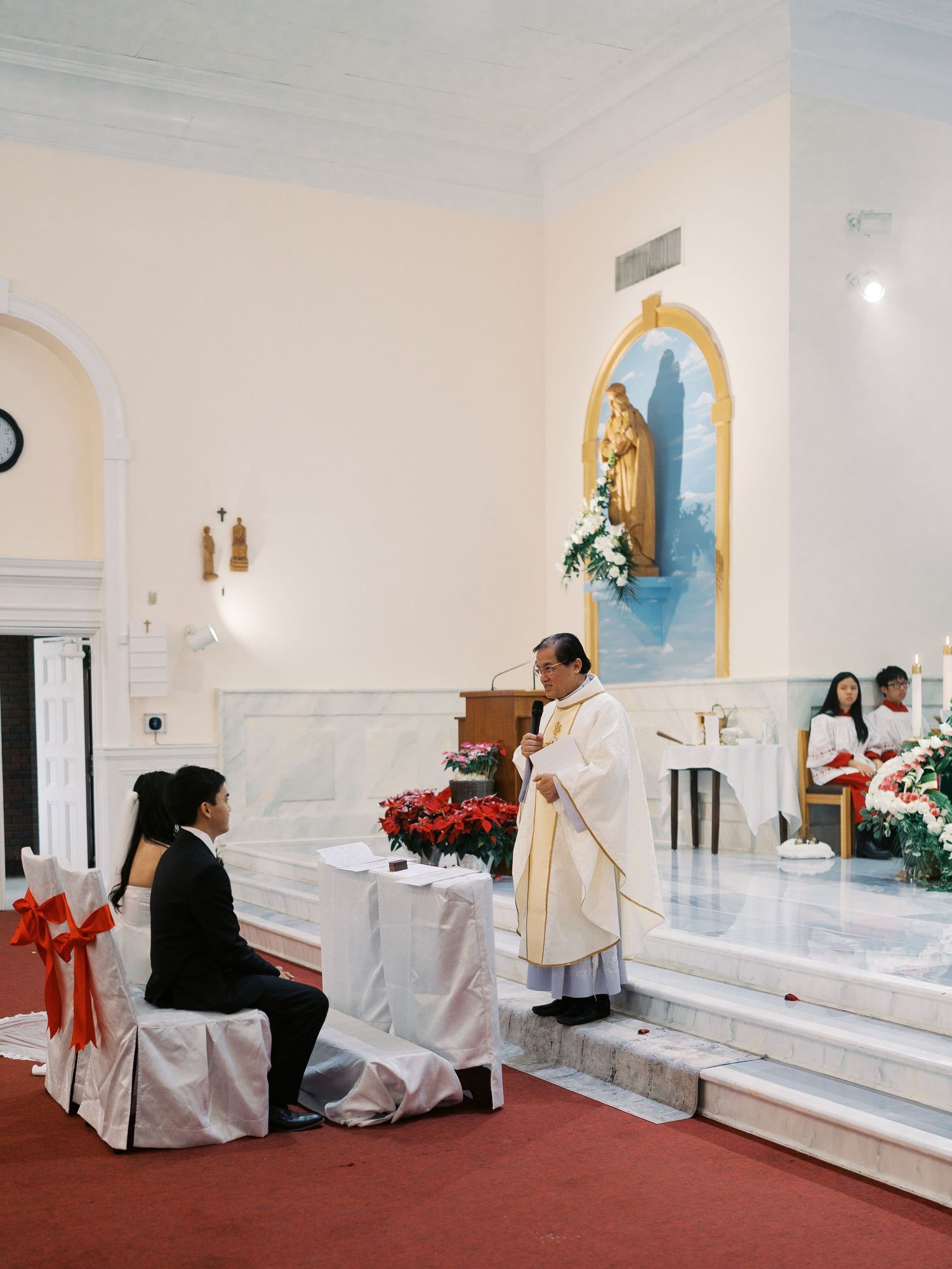 Church interior with white chairs and poinsettias decorated for a Christmas wedding ceremony.