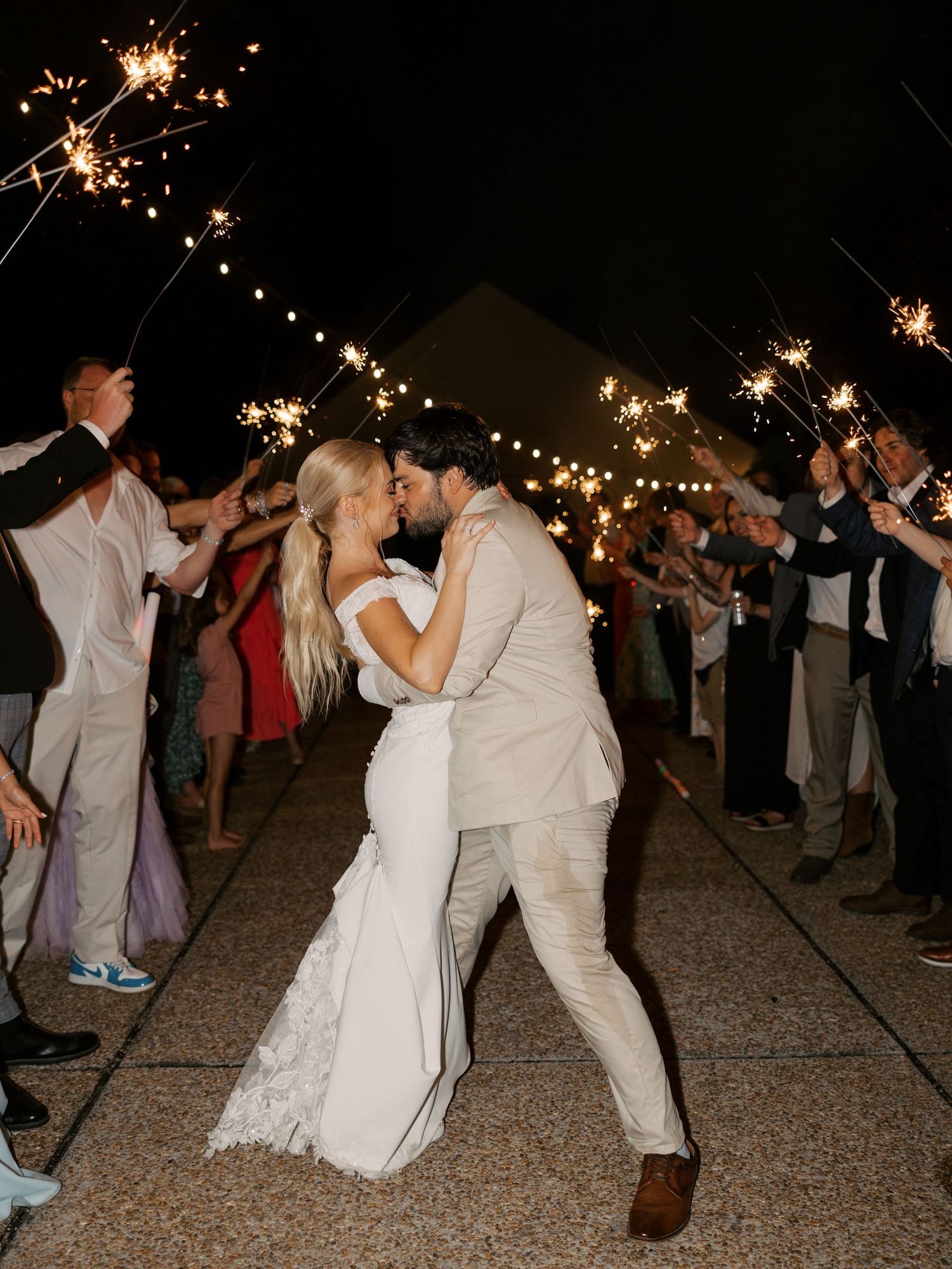 Wedding guests dance with sparklers during an outdoor nighttime celebration.