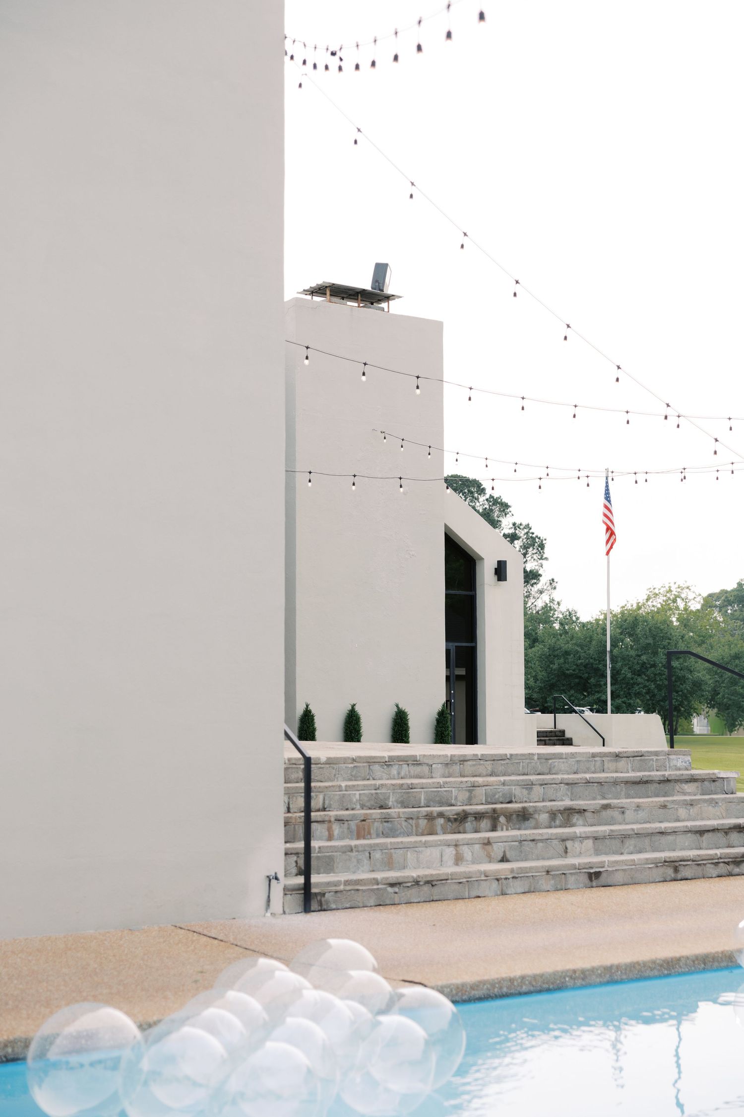 Modern white wedding venue with string lights and American flag near a pool area.