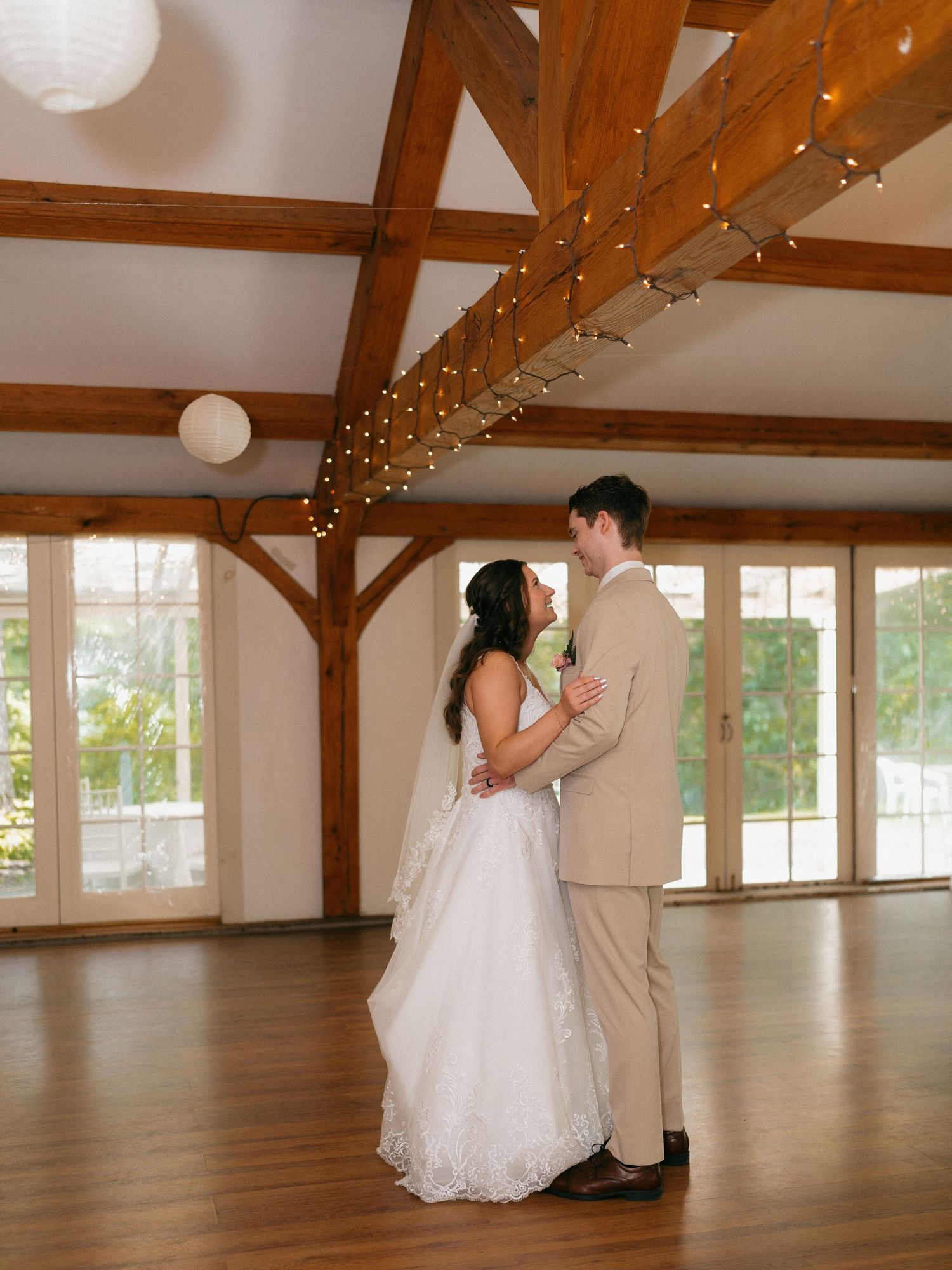 Couple dances in an elegant barn venue with wooden beams and large windows.