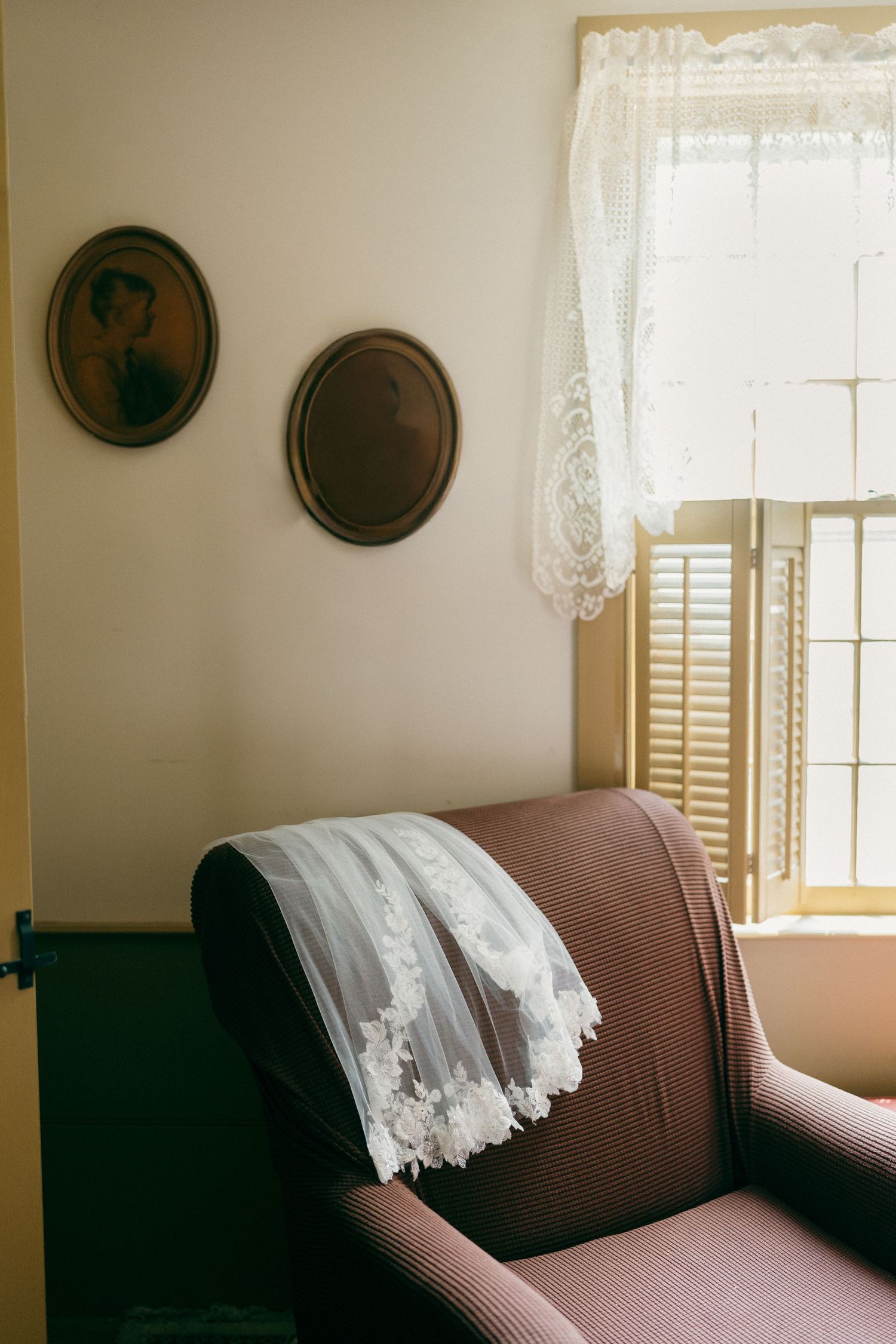 A cozy living room interior with lace curtains and decorative plates on beige walls.