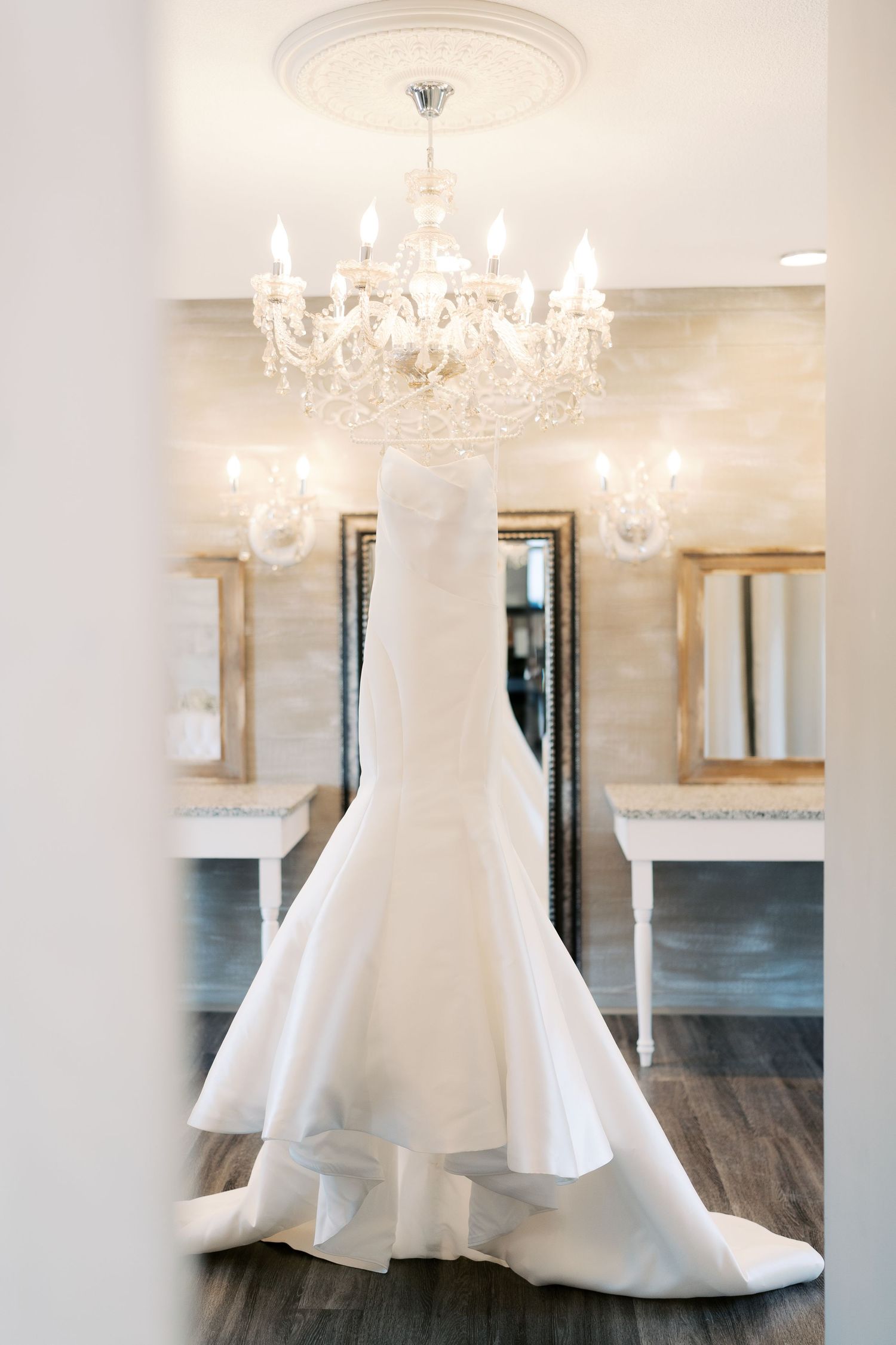 Elegant white wedding gown displayed in a room with crystal chandeliers and hardwood floors.