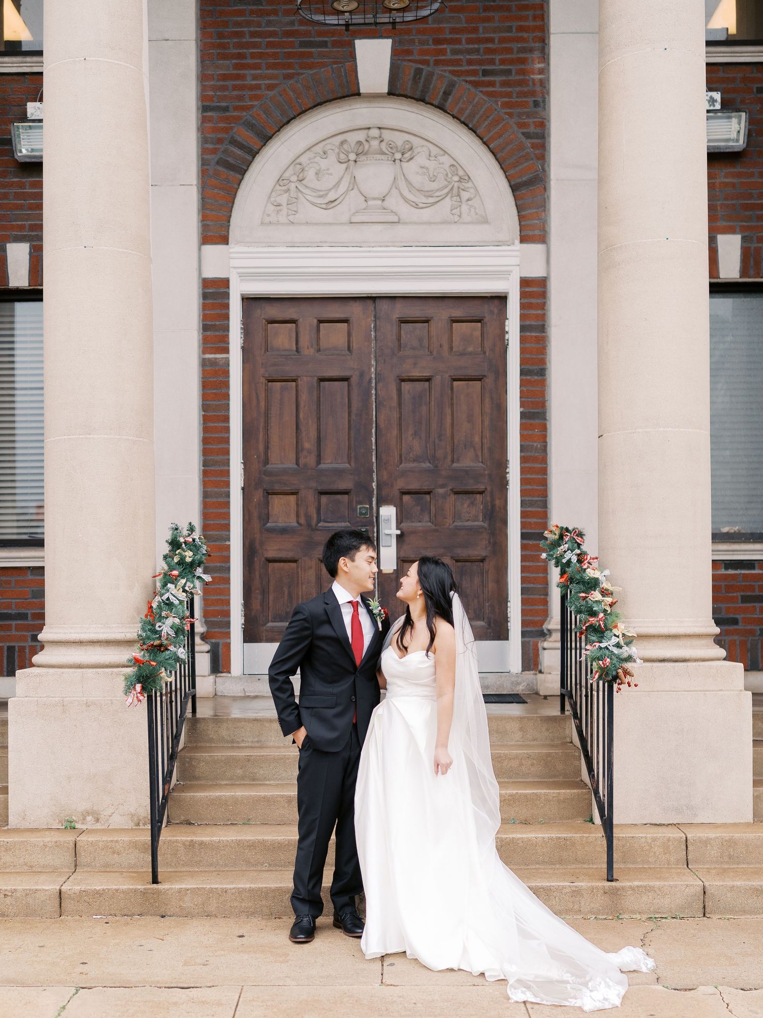 Wedding couple poses beneath classical stone archways and brick columns at historic venue.
