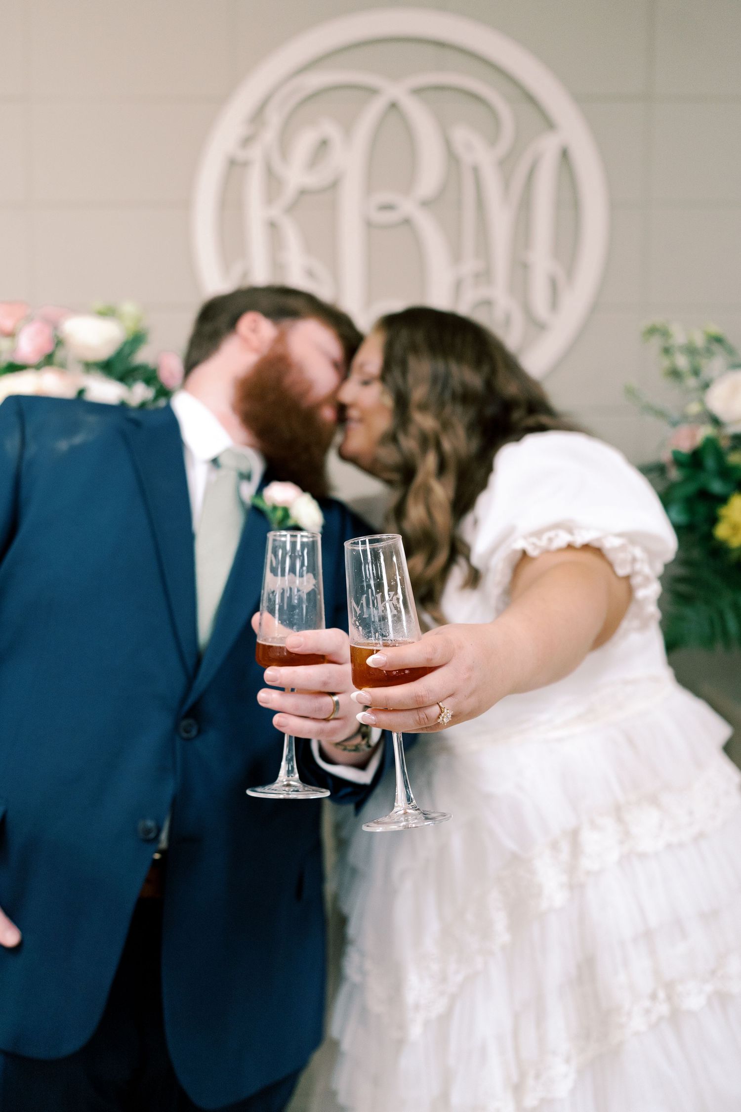 Newlyweds toasting with champagne glasses in front of a decorative white monogram wall.