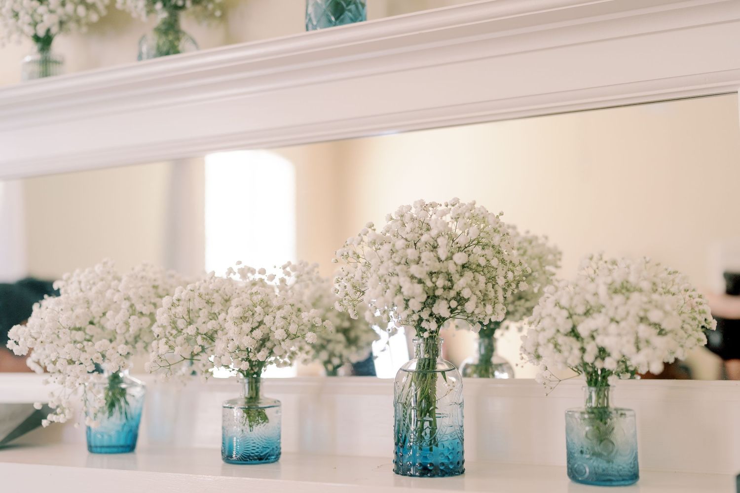 Row of blue glass vases filled with delicate baby's breath flowers for wedding decor.