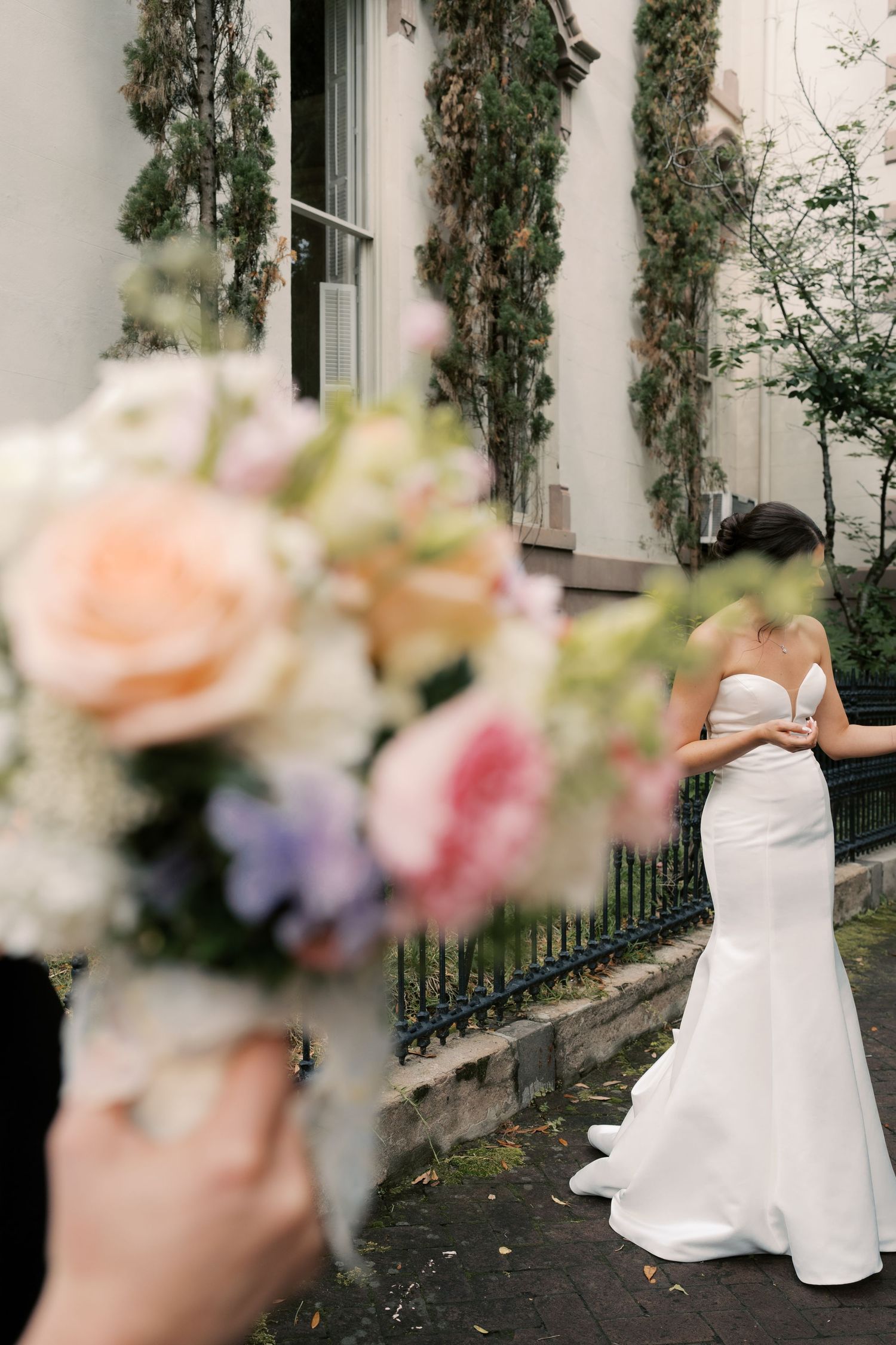 A white wedding dress with floral details is showcased against an ivy-covered wall.